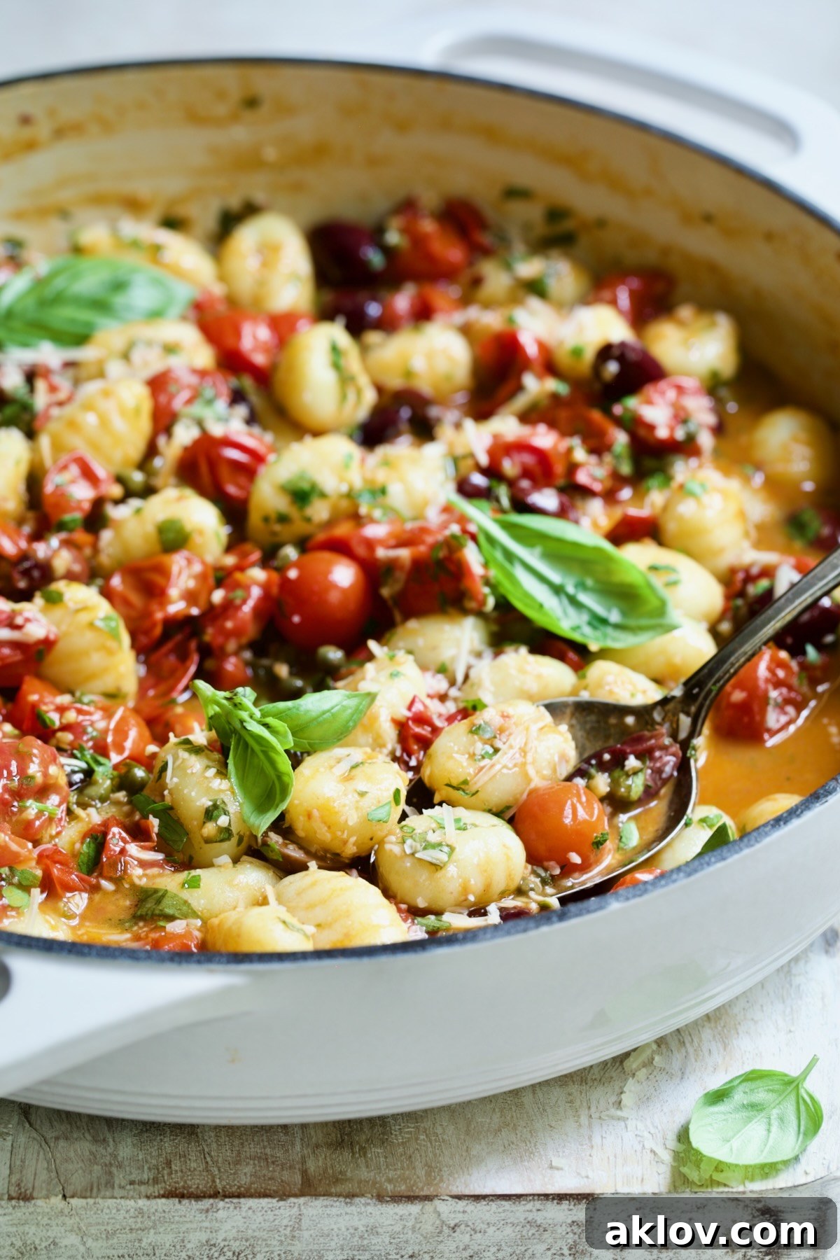 Gnocchi with Cherry Tomato Puttanesca Sauce in white enamel cast iron skillet with some on serving spoon.