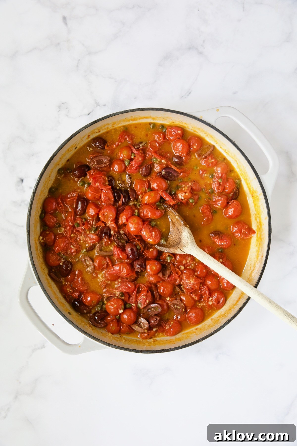 Cherry tomatoes and olives being stirred with wooden spoon.