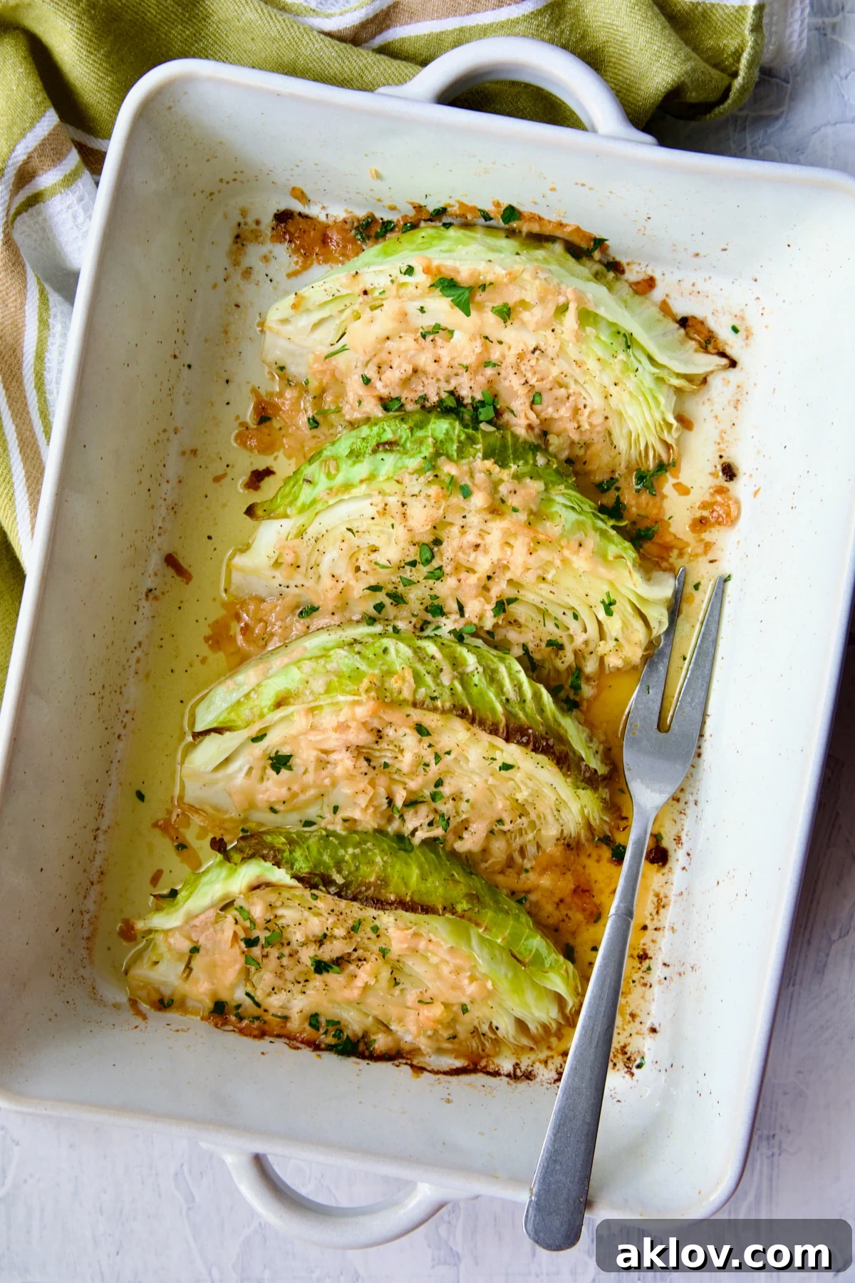 Baked Garlic Parmesan Cabbage Wedges in a white baking dish, ready to be served with a fork.