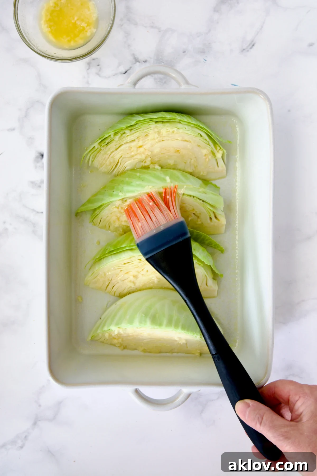 Four wedges of cabbage in white baking dish being brushed with butter and garlic.