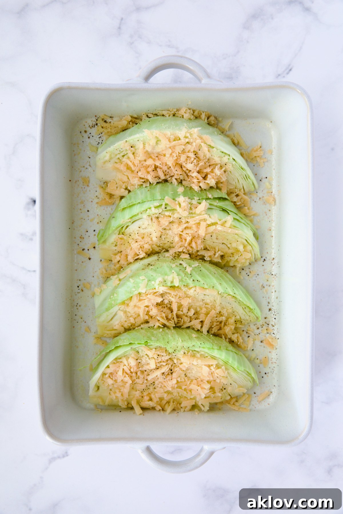 Four cabbage wedges neatly arranged in a white rectangular baking dish, generously sprinkled with Parmesan cheese.