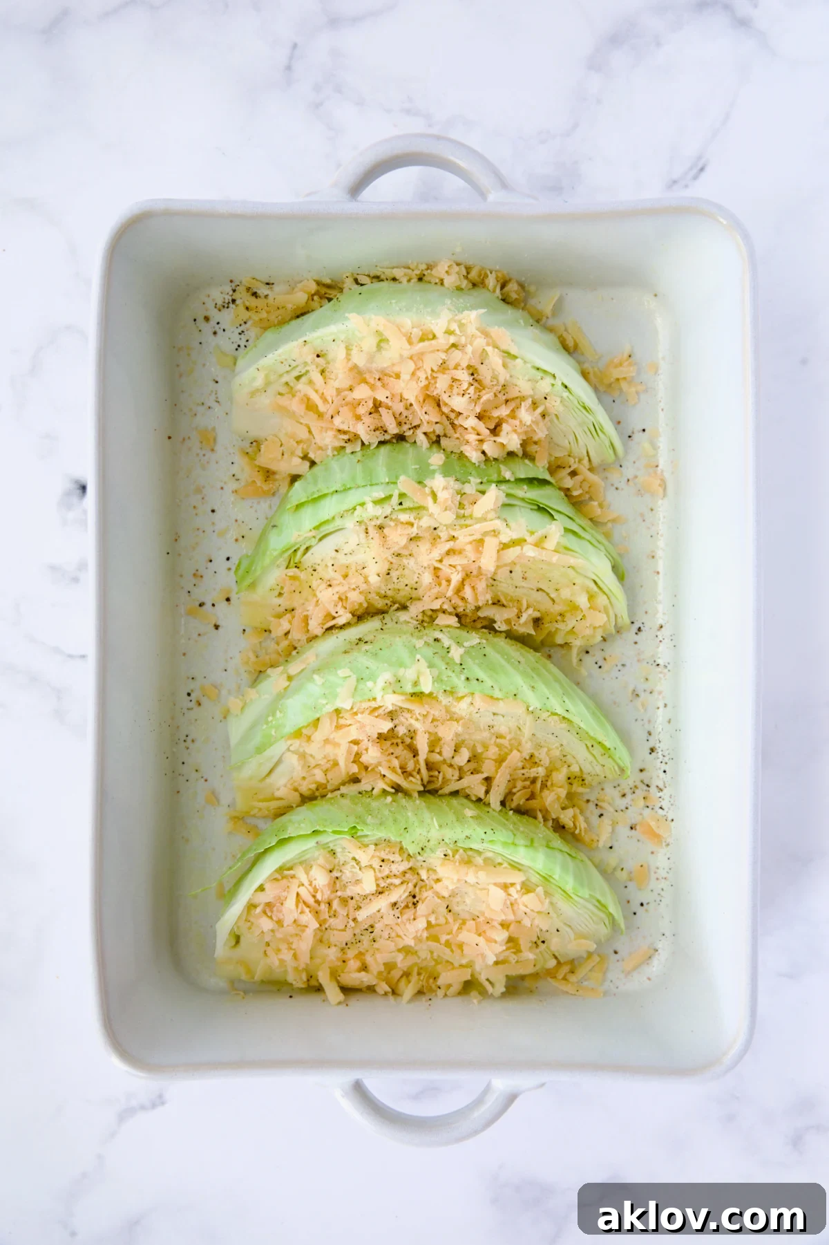 Four wedges of cabbage in white rectangular baking dish sprinkled with Parmesan cheese.