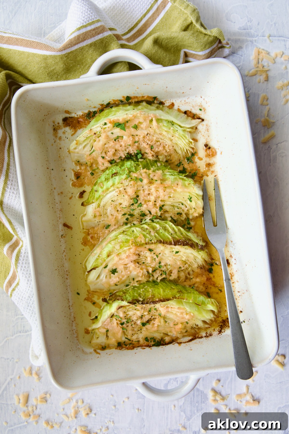 Baked Garlic Parmesan Cabbage Wedges freshly removed from the oven, served in a white rectangular baking dish with a serving fork and a green striped towel.
