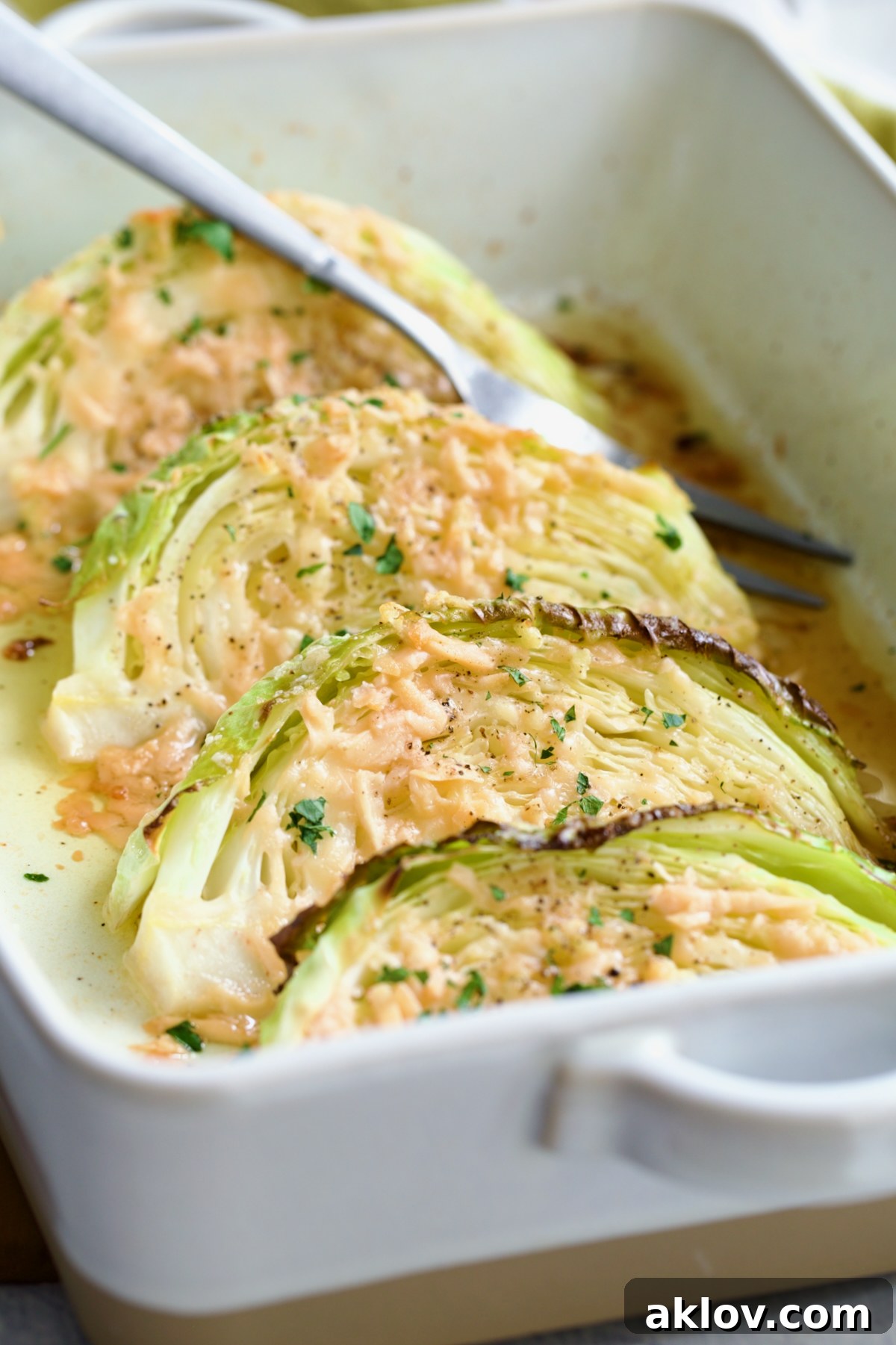 Four wedges of Baked Garlic Parmesan Cabbage Wedges in a baking dish with a serving fork, garnished with fresh chopped parsley.