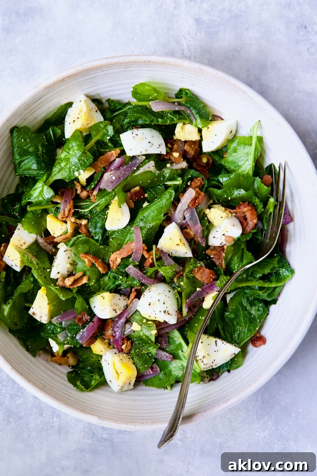 Fresh Radish Greens Salad with Hot Bacon Dressing, beautifully presented in a white serving bowl with a serving fork, highlighting its vibrant colors and crisp texture.