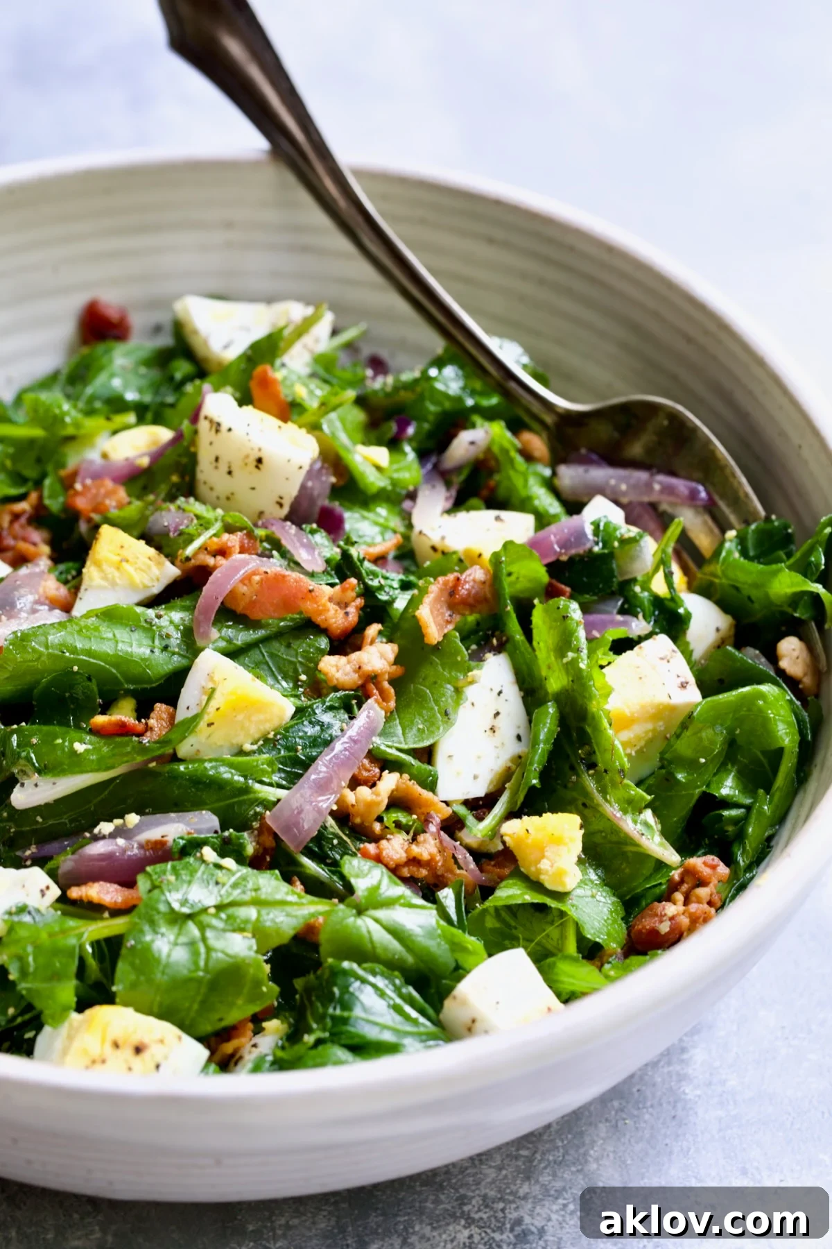 Radish Greens Salad with Hot Bacon Dressing presented in a large white serving bowl with a stylish serving fork, ready for dining.