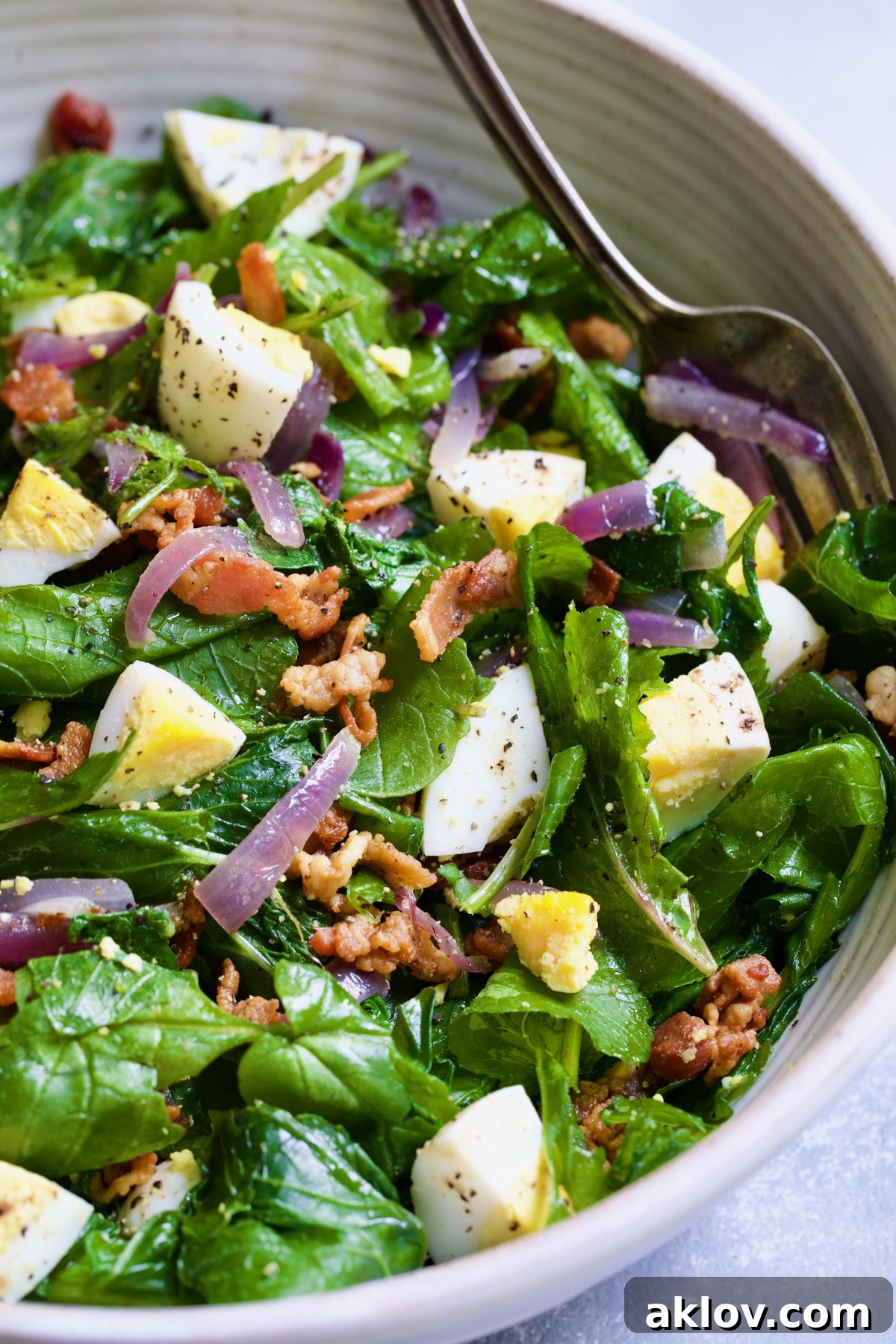 Close-up shot of Radish Greens Salad with Hot Bacon Dressing in a pristine white serving bowl, showcasing the tender greens, crispy bacon, and sliced hard-boiled eggs.