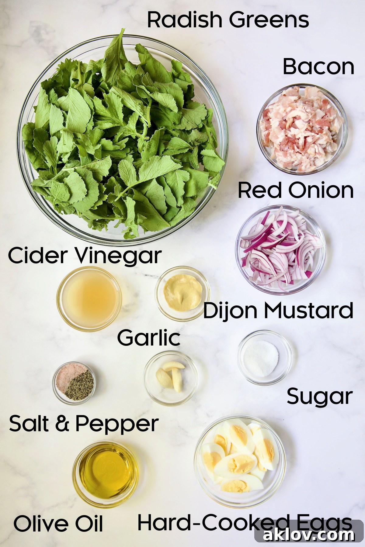 A selection of fresh ingredients for Radish Greens Salad with Hot Bacon Dressing, including crisp radish greens, bacon, red onion, garlic, and eggs, arranged in clear glass bowls.