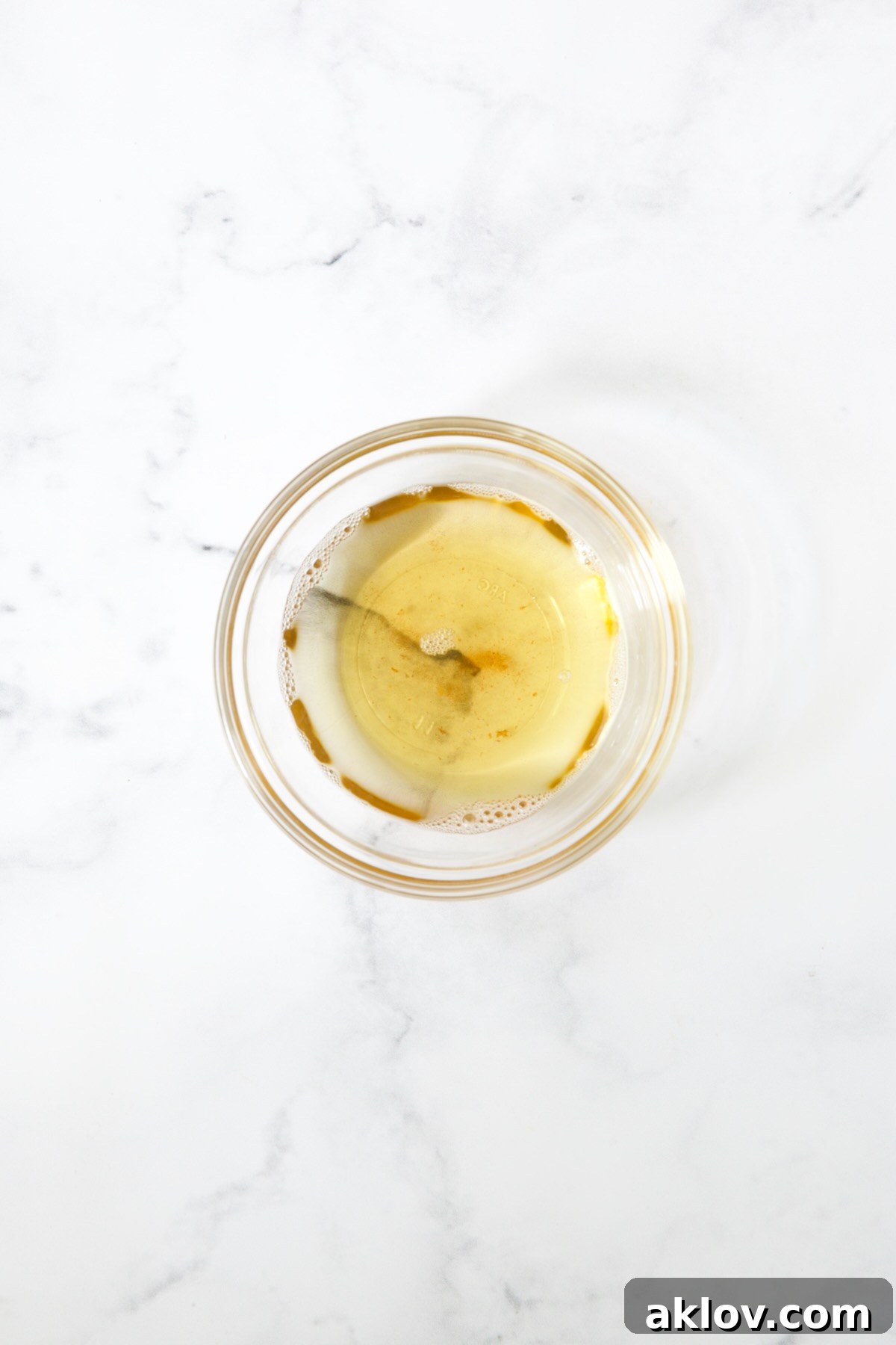 Measured bacon grease, a rich golden liquid, collected in a clear glass bowl, ready for the hot bacon dressing.