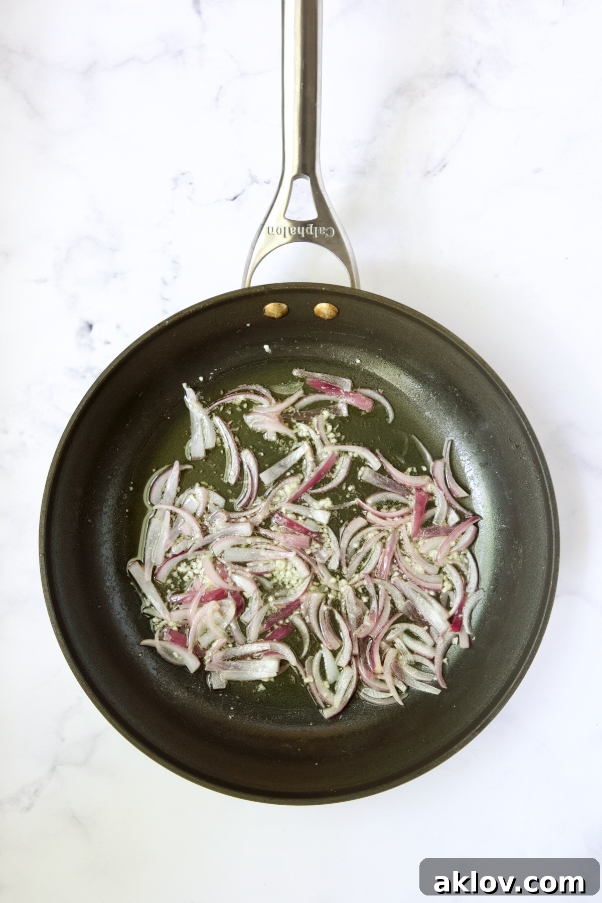 Thinly sliced red onions and minced garlic gently sautéing in bacon fat within a nonstick skillet, filling the air with their delicious aroma.