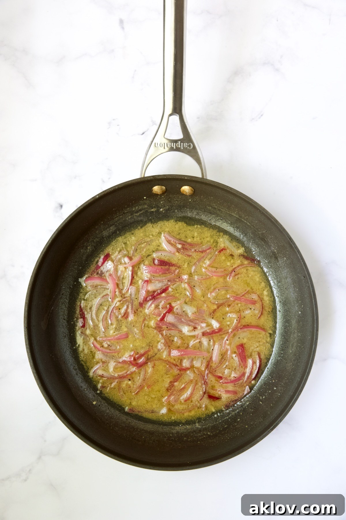 The vibrant hot bacon dressing, a rich brown liquid with sautéed onions, simmering gently in a skillet, ready to be combined with fresh greens.