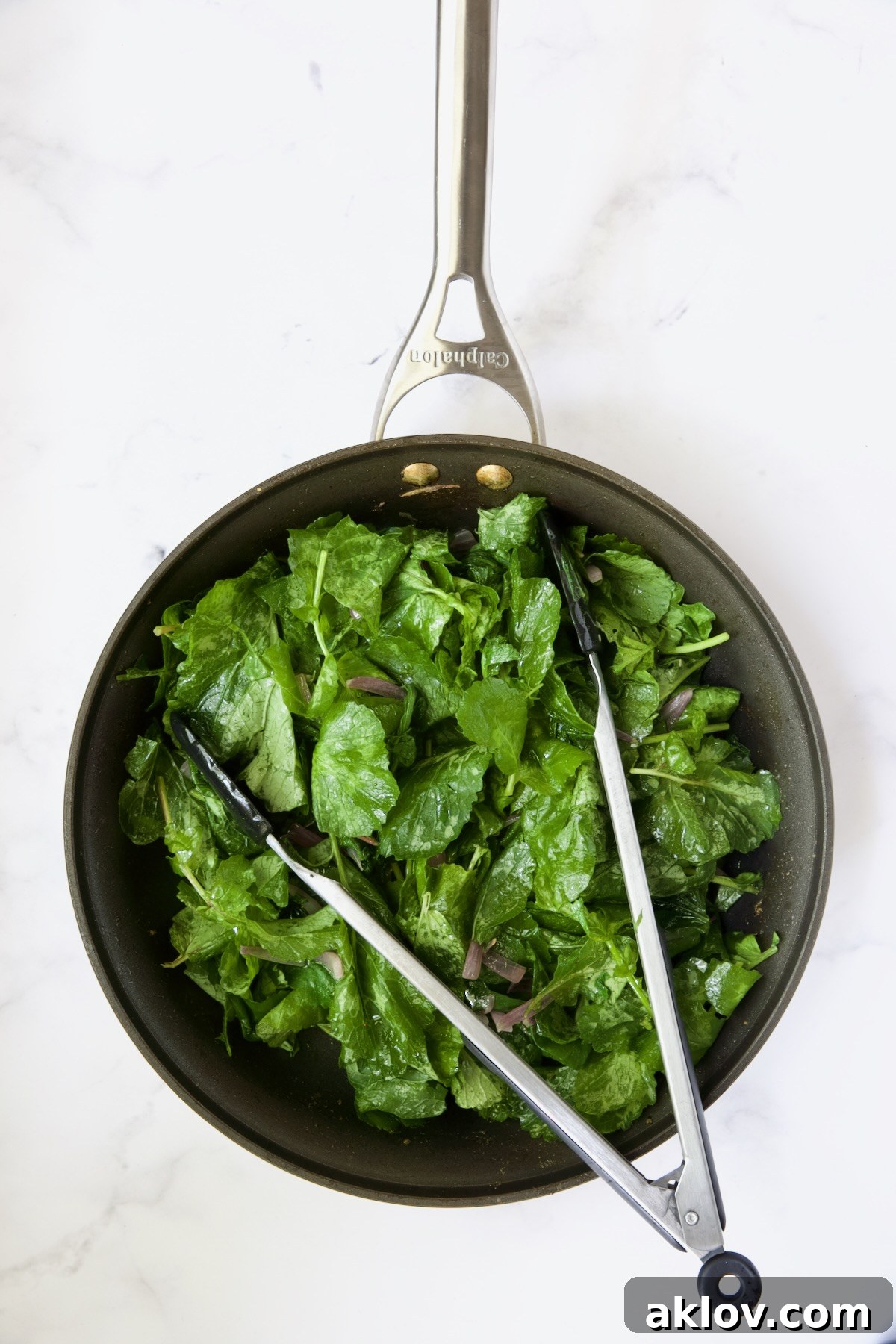 Tender radish greens, slightly wilted by the warm dressing, being tossed with tongs in a skillet, showcasing their vibrant green color.