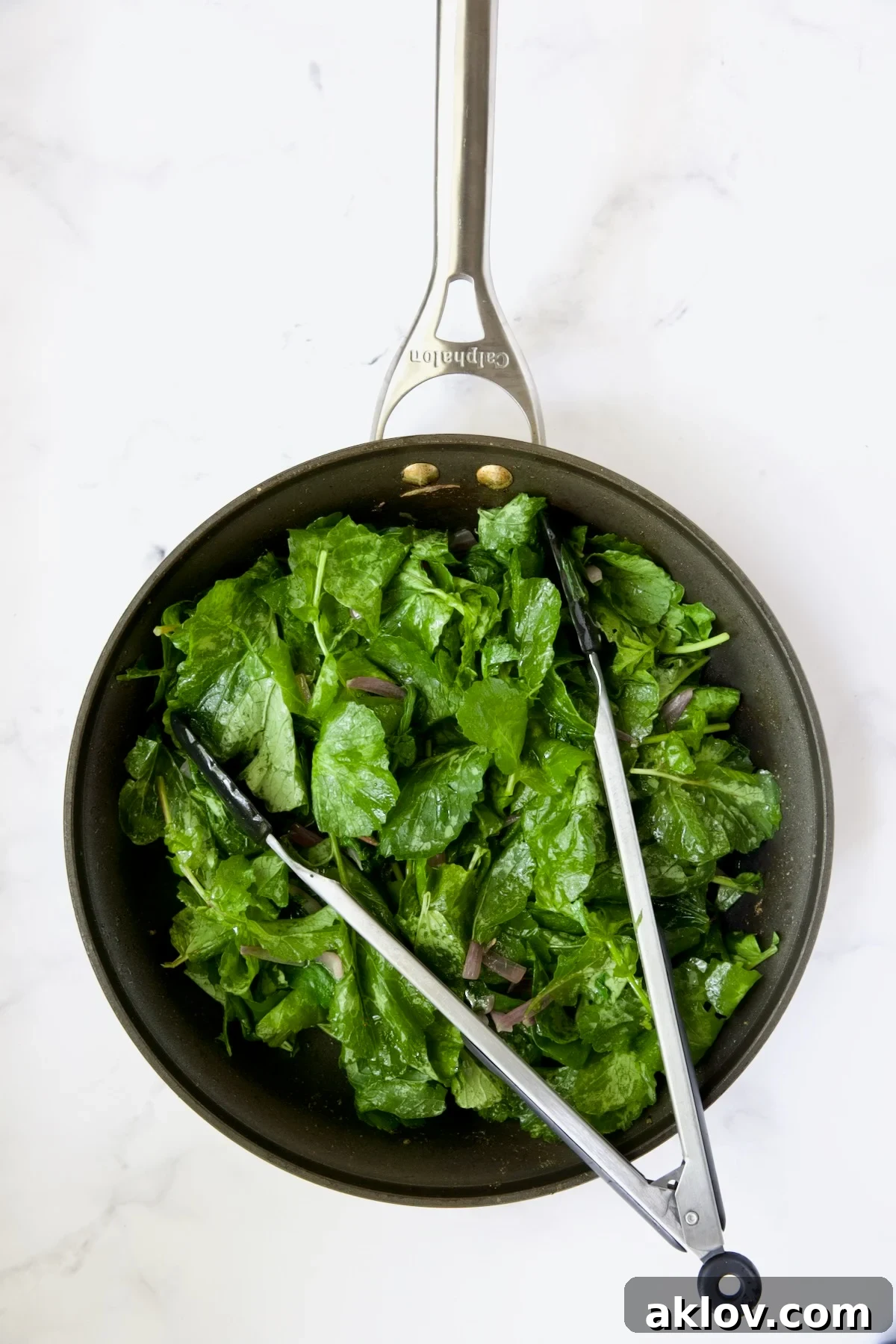 Slightly wilted radish greens being tossed with tongs in a skillet.
