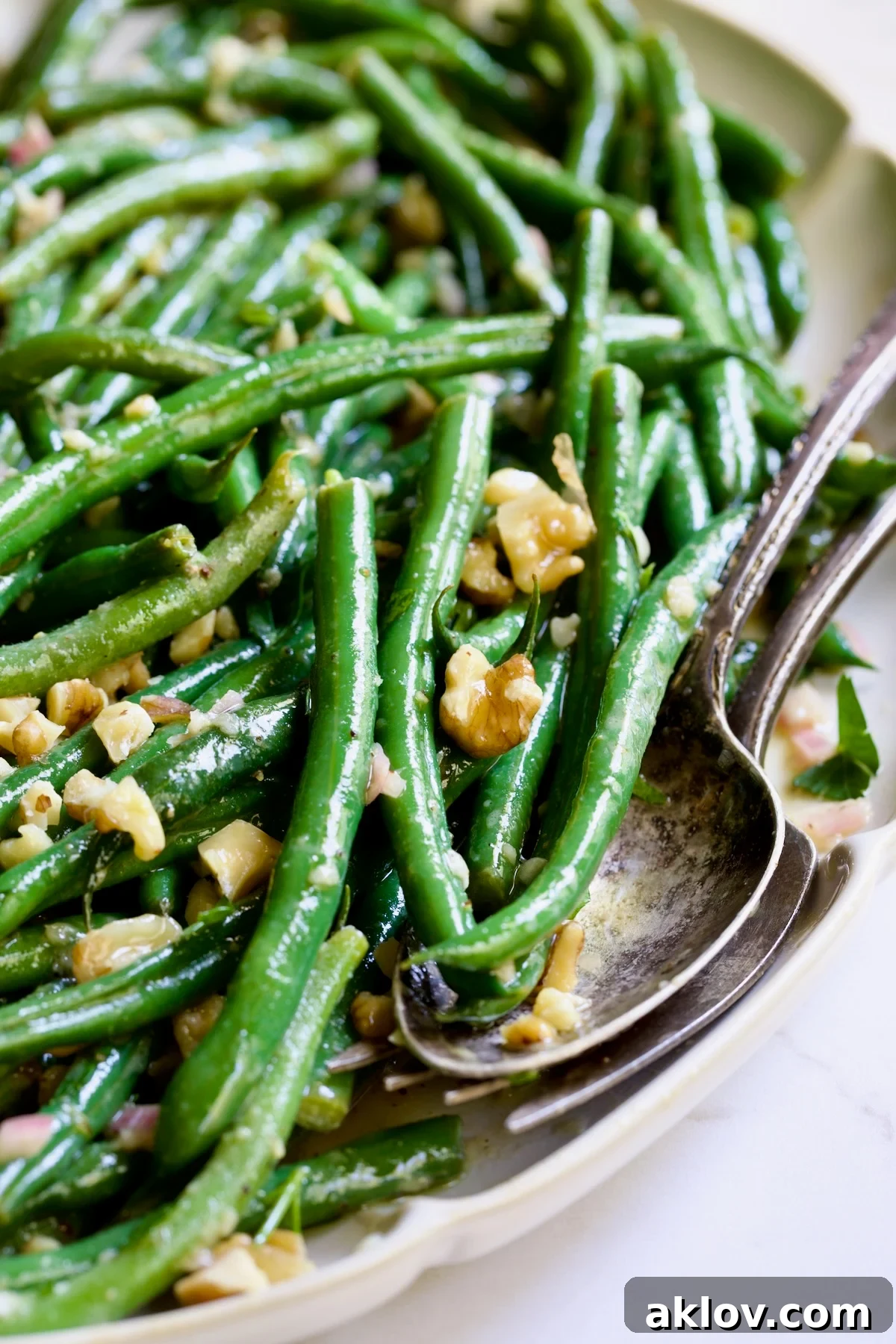 Green Bean Salad with Mustard Vinaigrette on white oval platter with serving utensils garnished with walnuts.