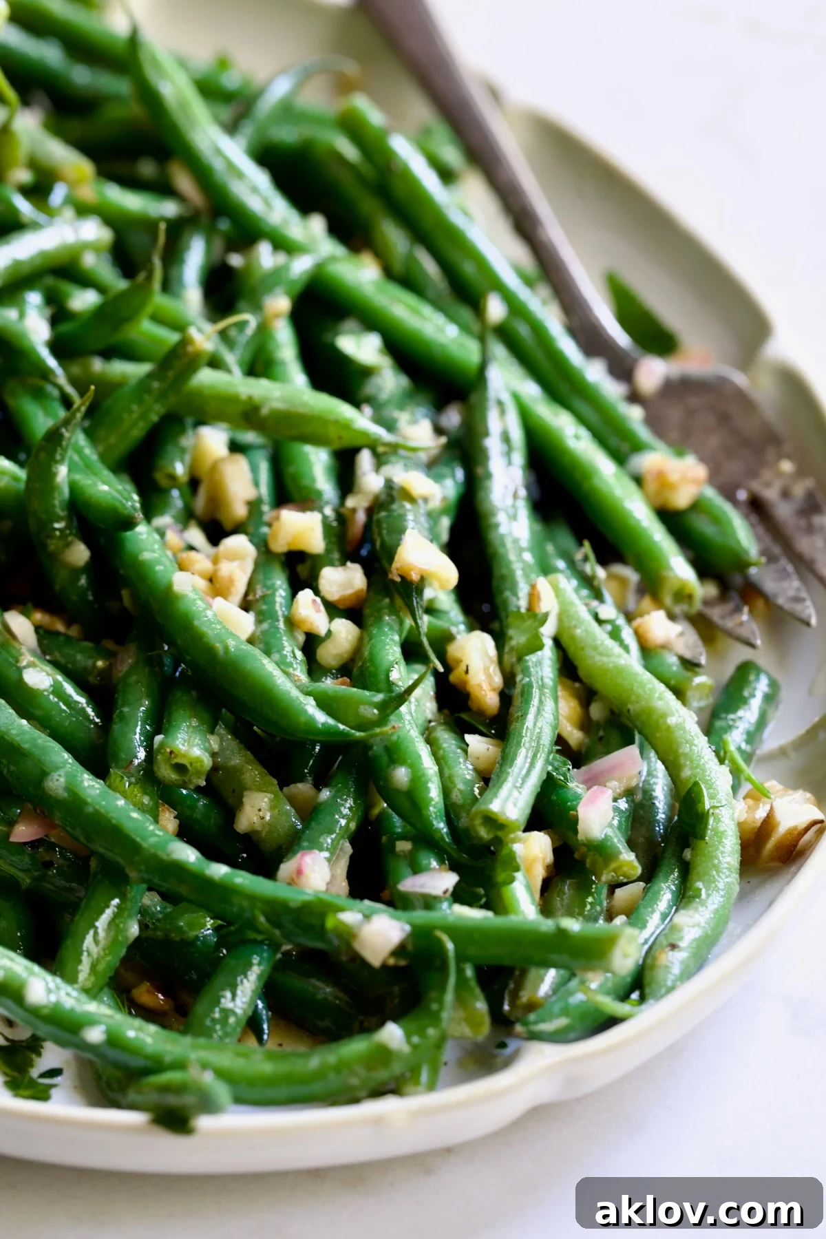 Green Bean Salad with Mustard Vinaigrette on white oval platter with serving utensils garnished with walnuts.