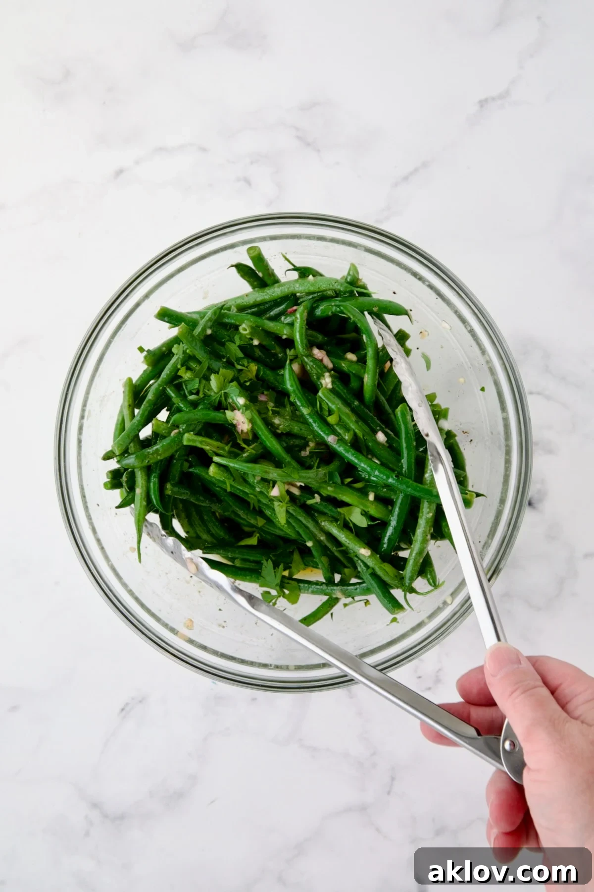 Green beans being tossed with vinaigrette in glass bowl.