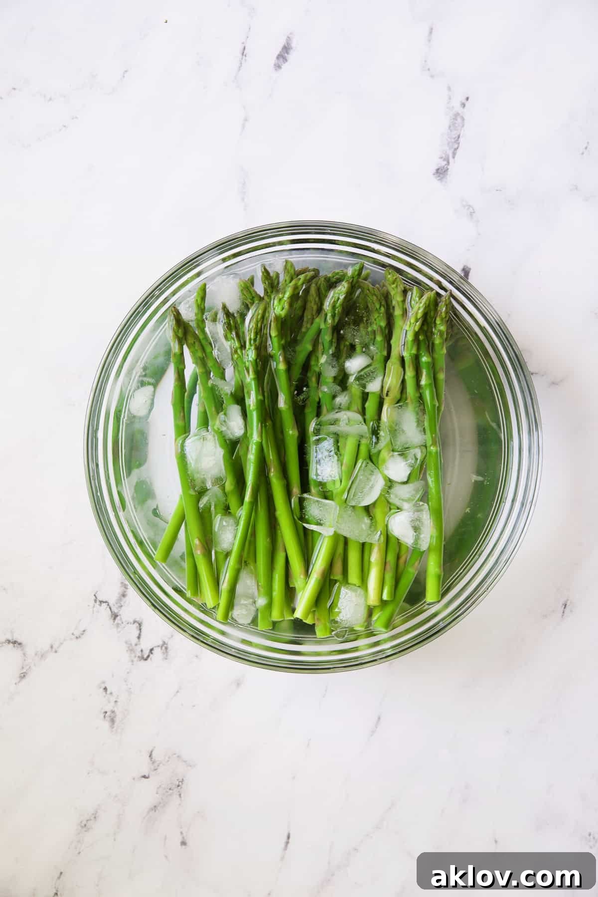 Photo of asparagus in ice bath in glass bowl.