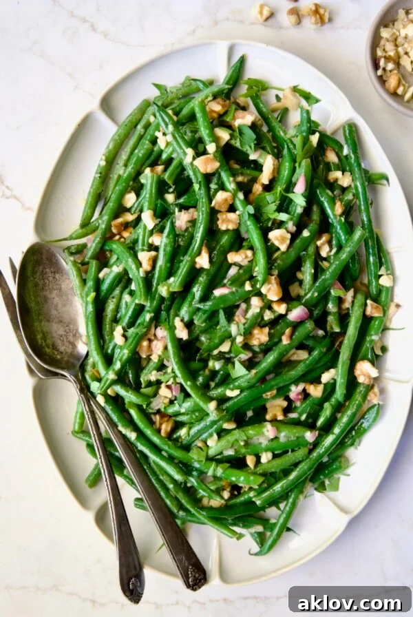 Green Bean Salad with Mustard Vinaigrette served on a white oval platter and garnished with crunchy walnuts.