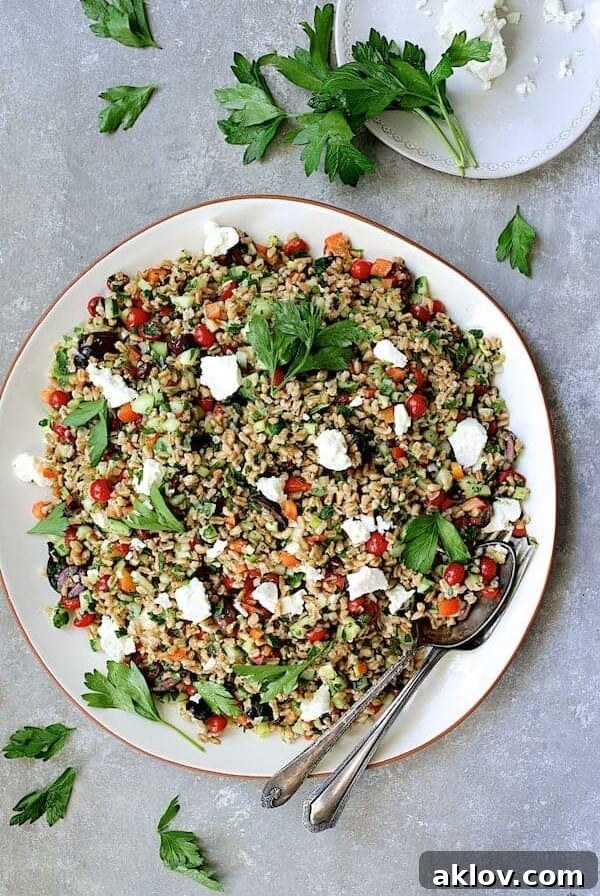 Mediterranean Farro Salad elegantly arranged on a round white platter with serving utensils and garnished with fresh parsley.
