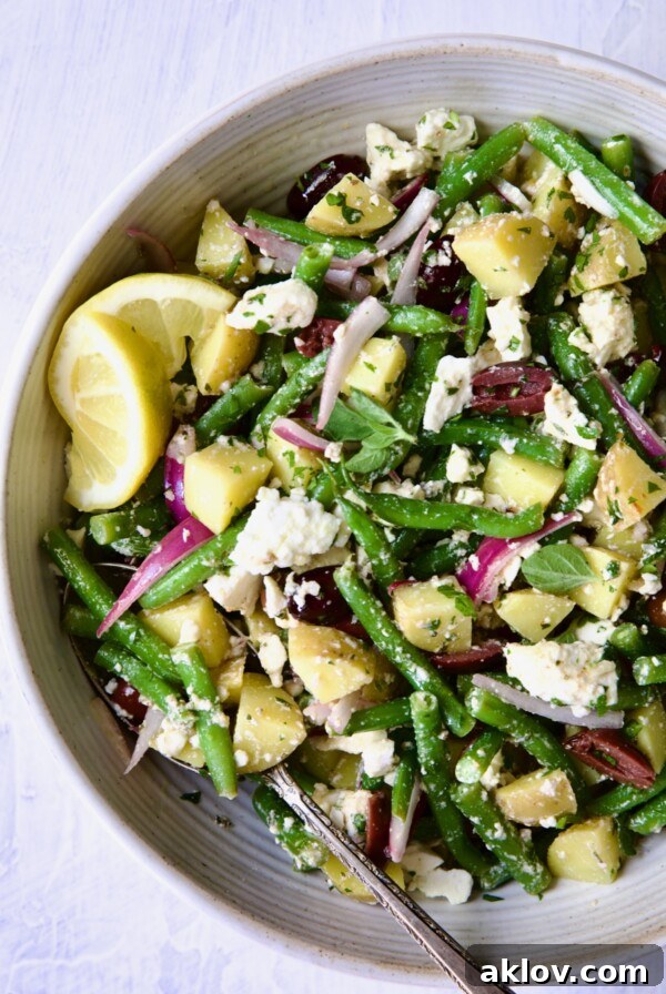 Potato Green Bean Salad served in a pristine white bowl, garnished with bright lemon wedges.