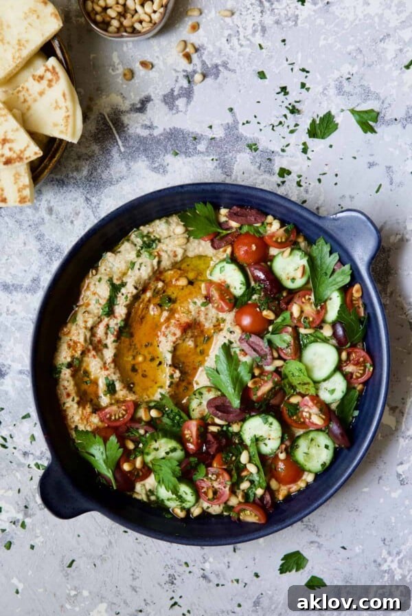Loaded Roasted Eggplant Dip (Baba Ganoush) in a beautiful blue dish with toasted pita wedges and a sprinkle of pine nuts for garnish.