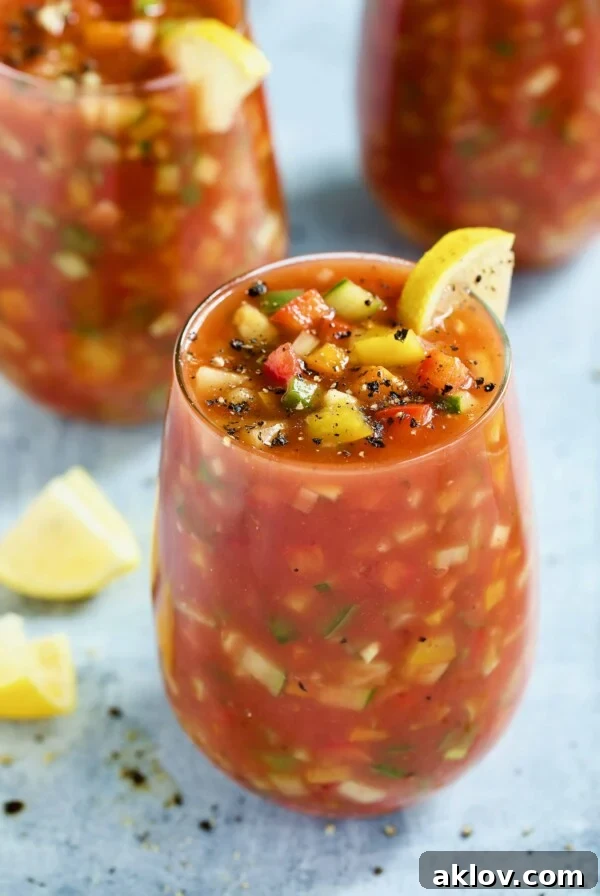 A refreshing glass of Very Veggie Gazpacho, beautifully garnished with bright lemon wedges, set against a light blue background.