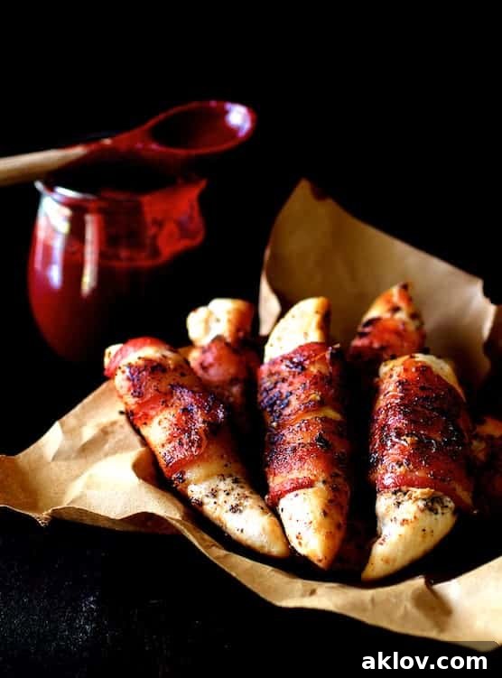 Sweet and Smoky Bacon Chicken Tenders with Raspberry Chipotle Glaze 2 Golden brown Bacon-Wrapped Chicken Tenders with a side of glossy Raspberry Chipotle Sauce, presented on rustic brown paper.