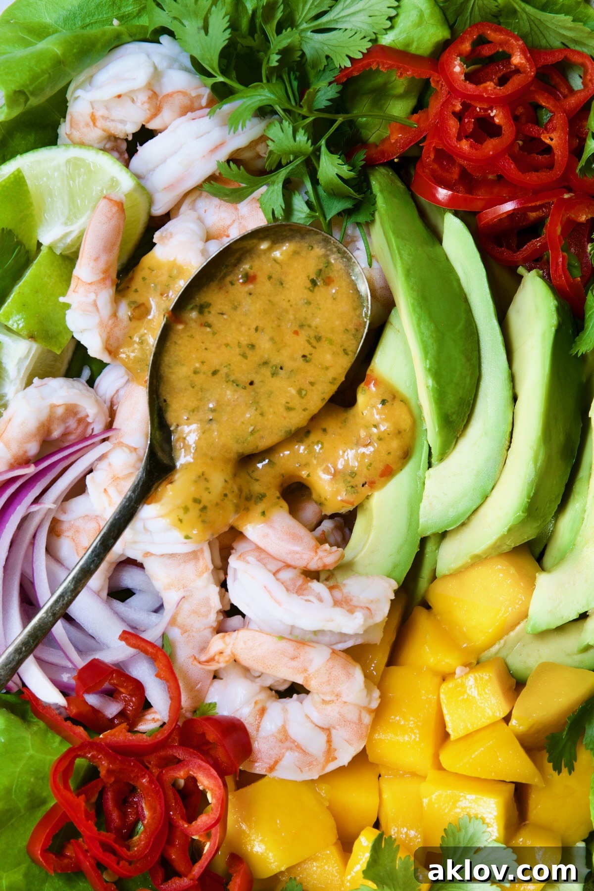A close-up shot of the sweet chili vinaigrette being spooned over the Butter Lettuce Salad with Shrimp, Mango, and Avocado, highlighting the rich texture of the dressing.