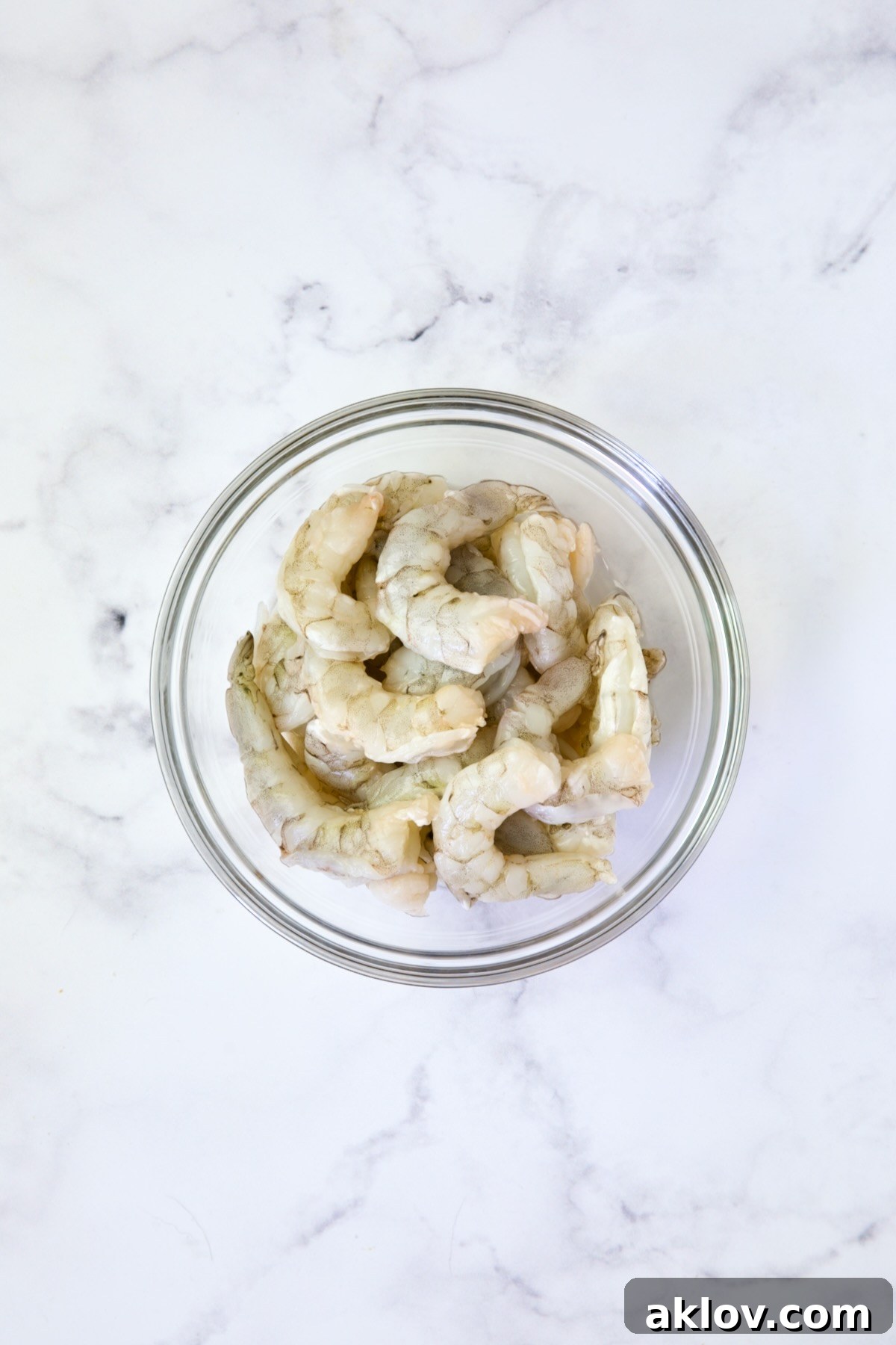 A glass bowl filled with raw, peeled, and deveined shrimp, ready for cooking, illustrating their fresh and translucent appearance.