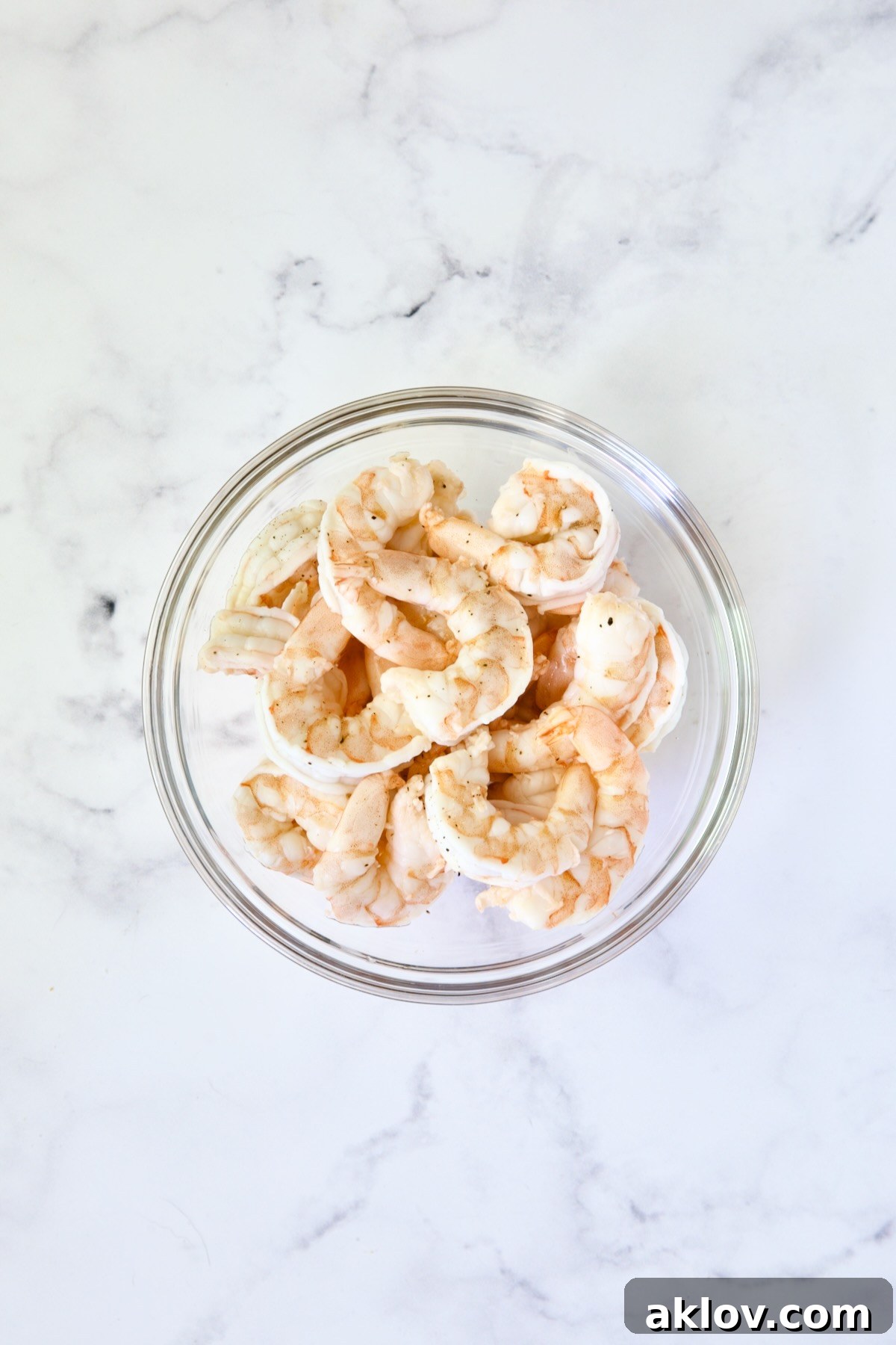 A glass bowl containing perfectly cooked shrimp, showing their appealing pink color and curled shape after being quickly cooled.