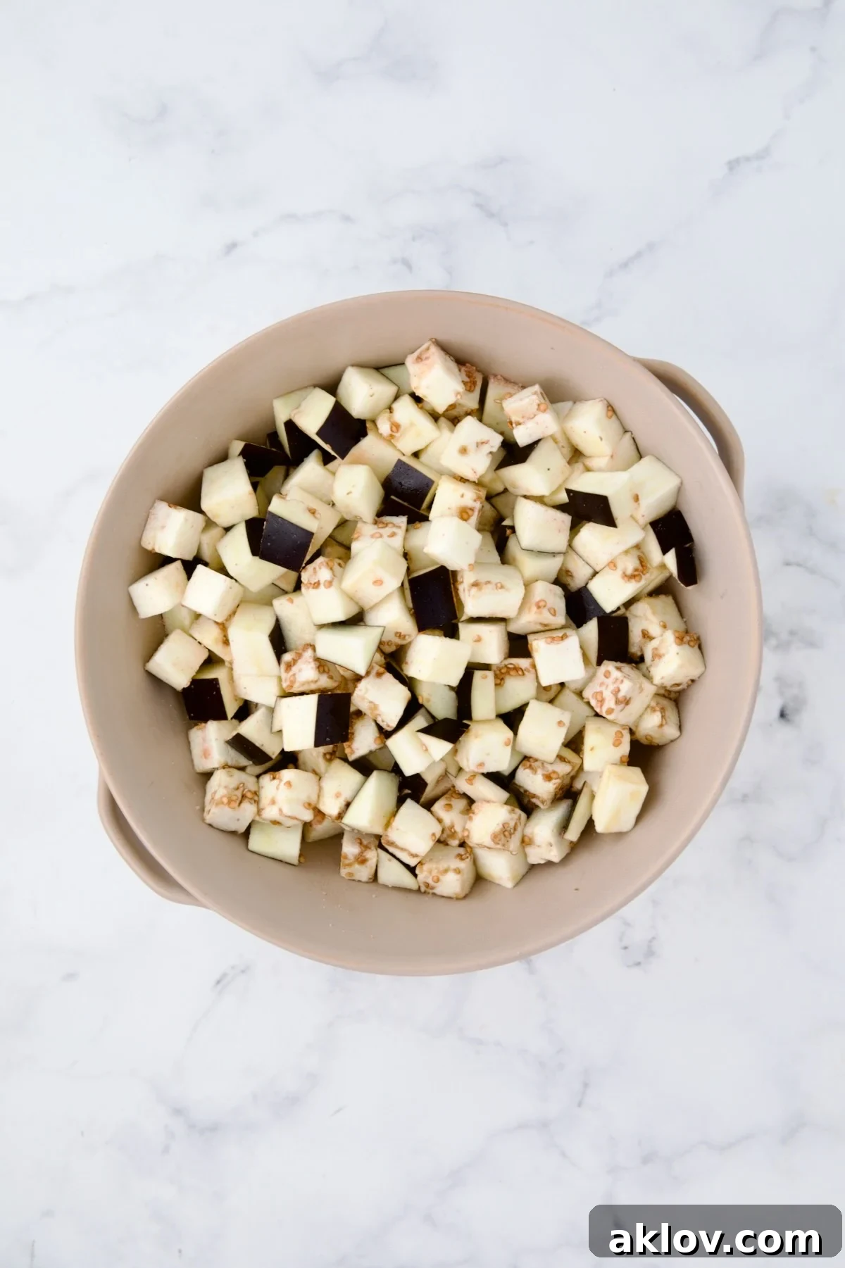 Cubed eggplant resting in a beige colander after being salted, allowing excess moisture to drain.
