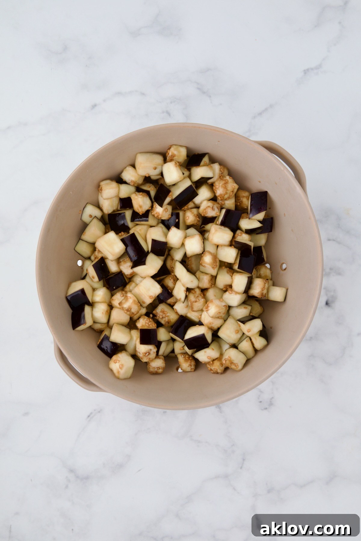 Cubes of eggplant in beige colander after being salted and drained.