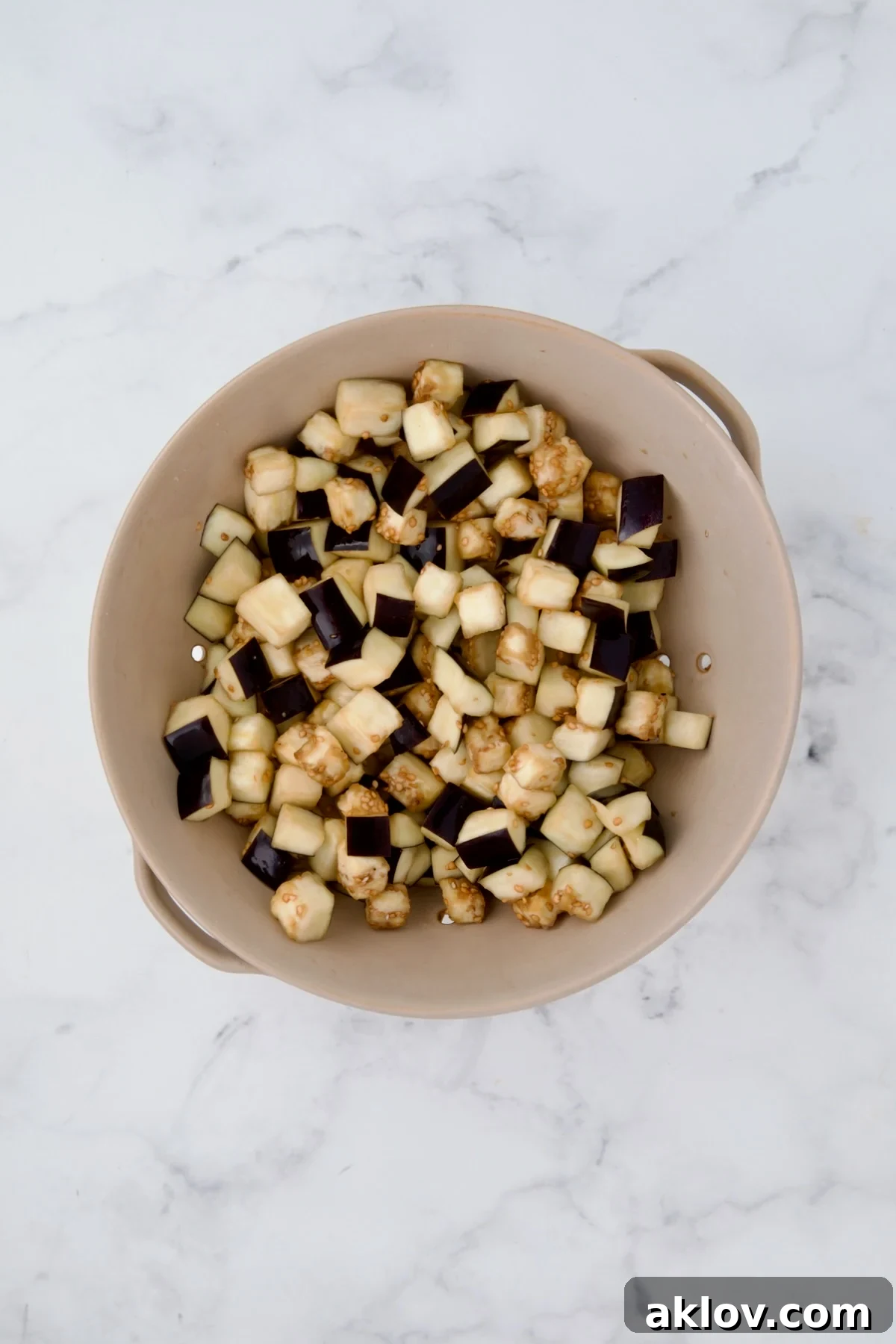 Salted and drained eggplant cubes in a beige colander, showing the moisture that has been drawn out.