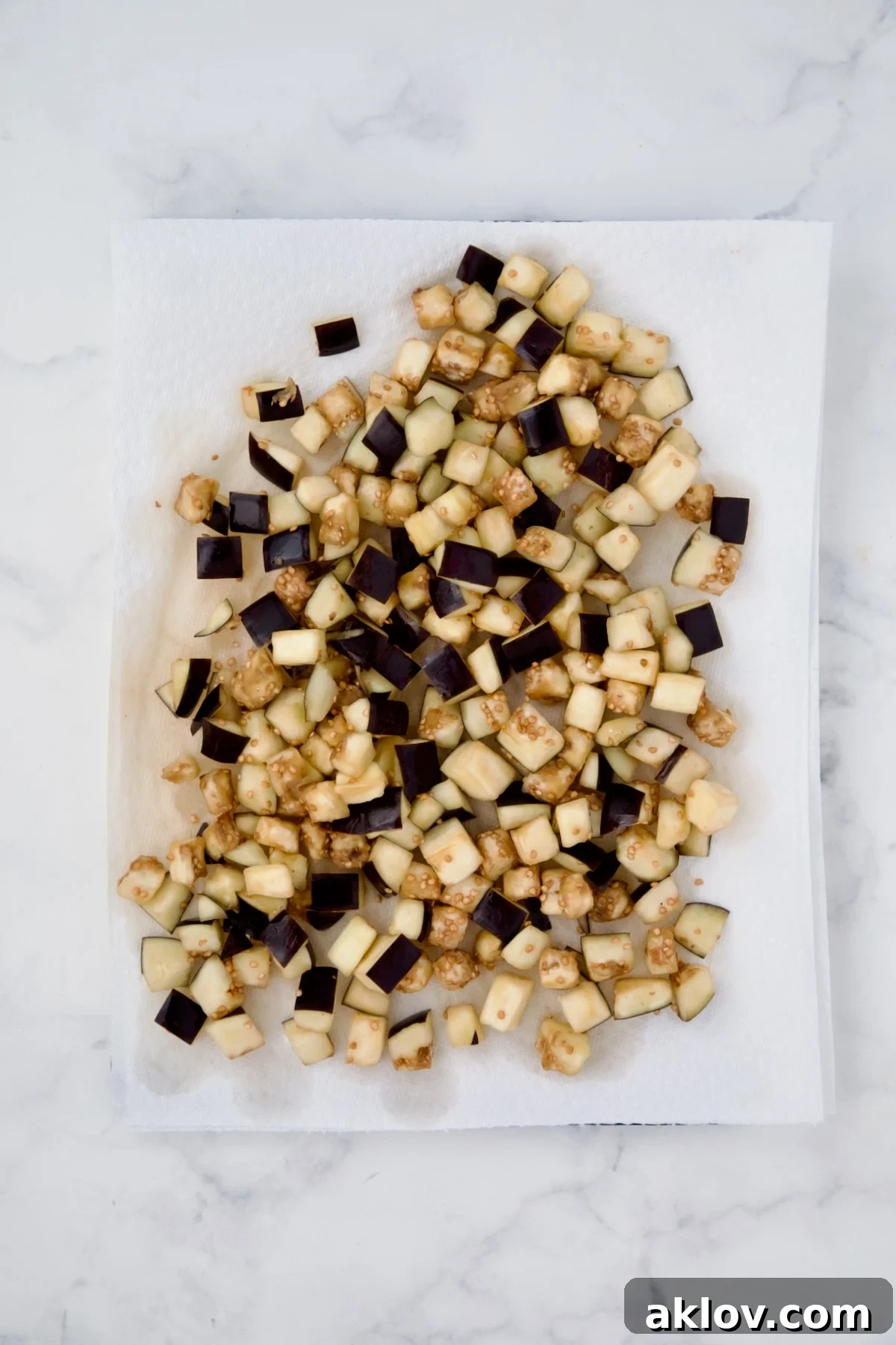 Cubed eggplant being gently dabbed dry with paper towels after salting and draining.