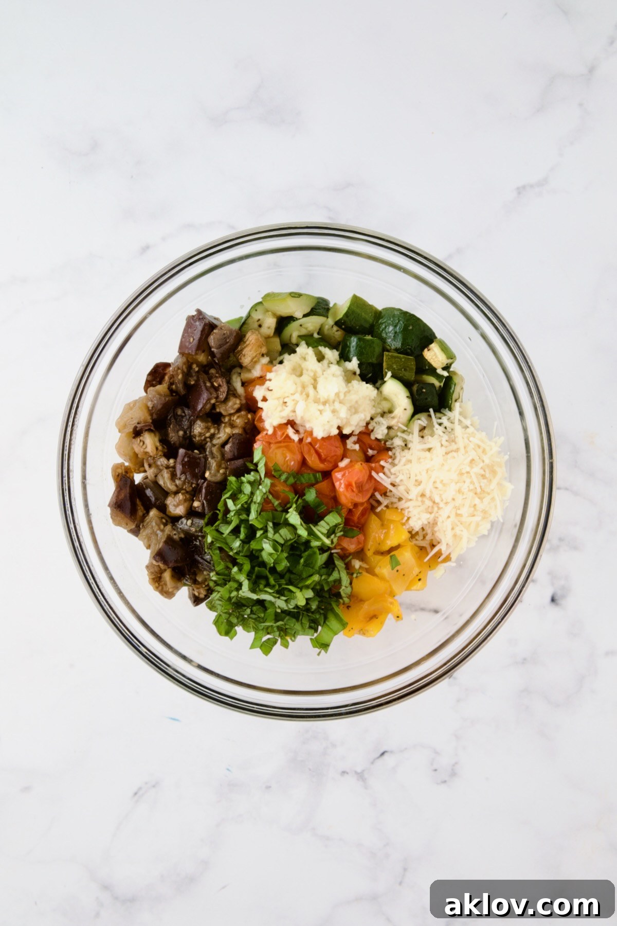 Roasted vegetables, shredded Parmesan cheese, and minced garlic in a glass mixing bowl, ready to be tossed together for the galette filling.