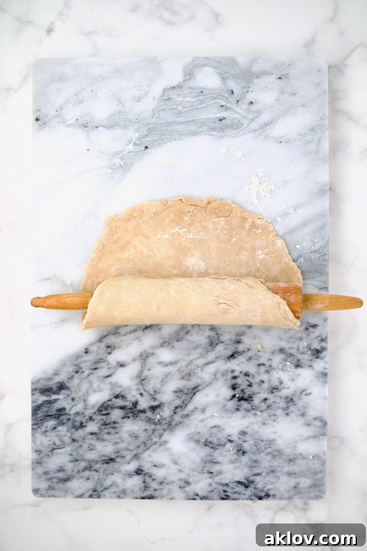 Galette dough on pastry board being rolled onto a rolling pin.