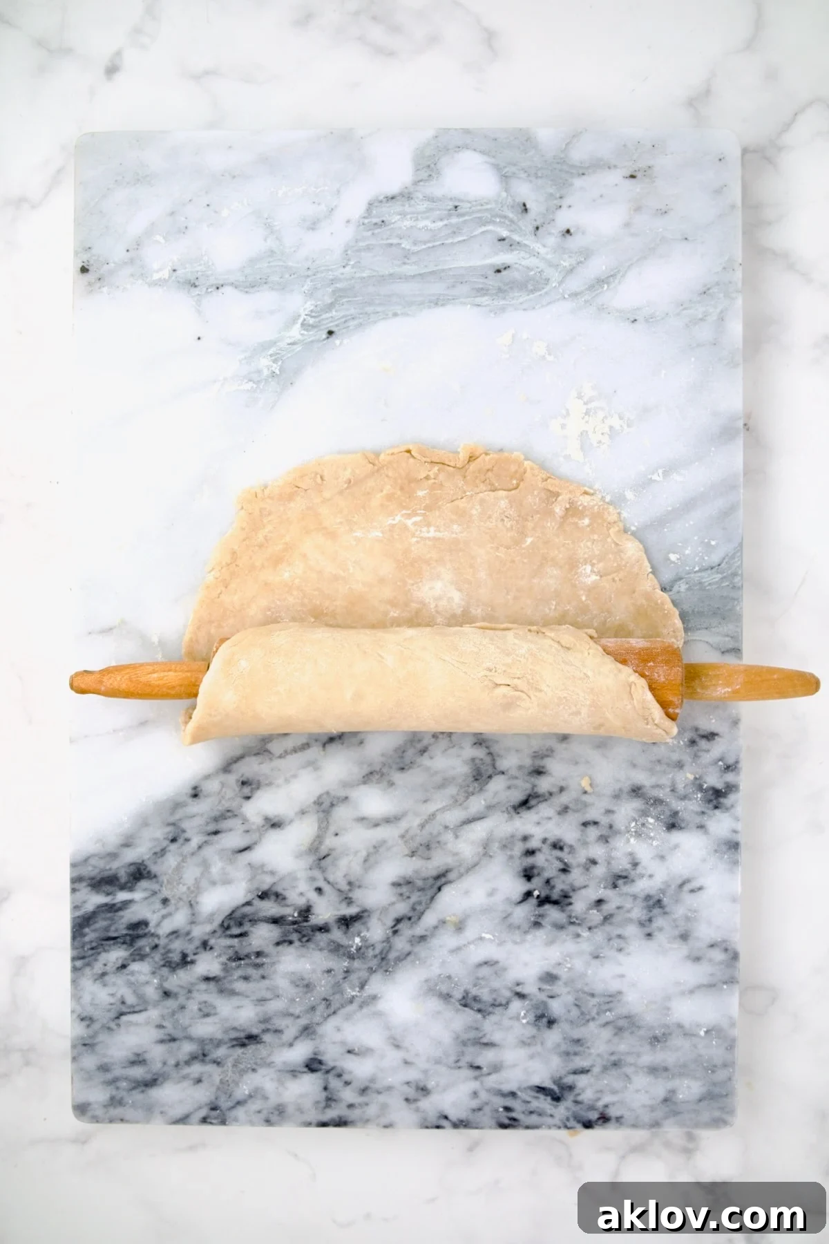 Rolled-out galette dough being gently transferred onto a rolling pin, demonstrating a technique for easy placement.