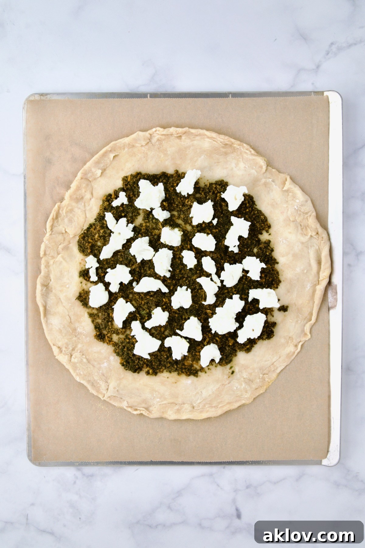 Rolled out galette dough on parchment paper on cookie sheet with pesto and goat cheese added.