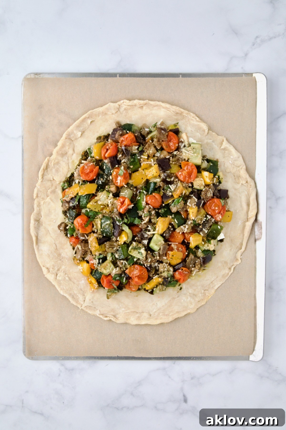 Roasted vegetables, pesto, and goat cheese neatly arranged on the rolled out galette dough on a parchment-lined cookie sheet, with the crust border visible.