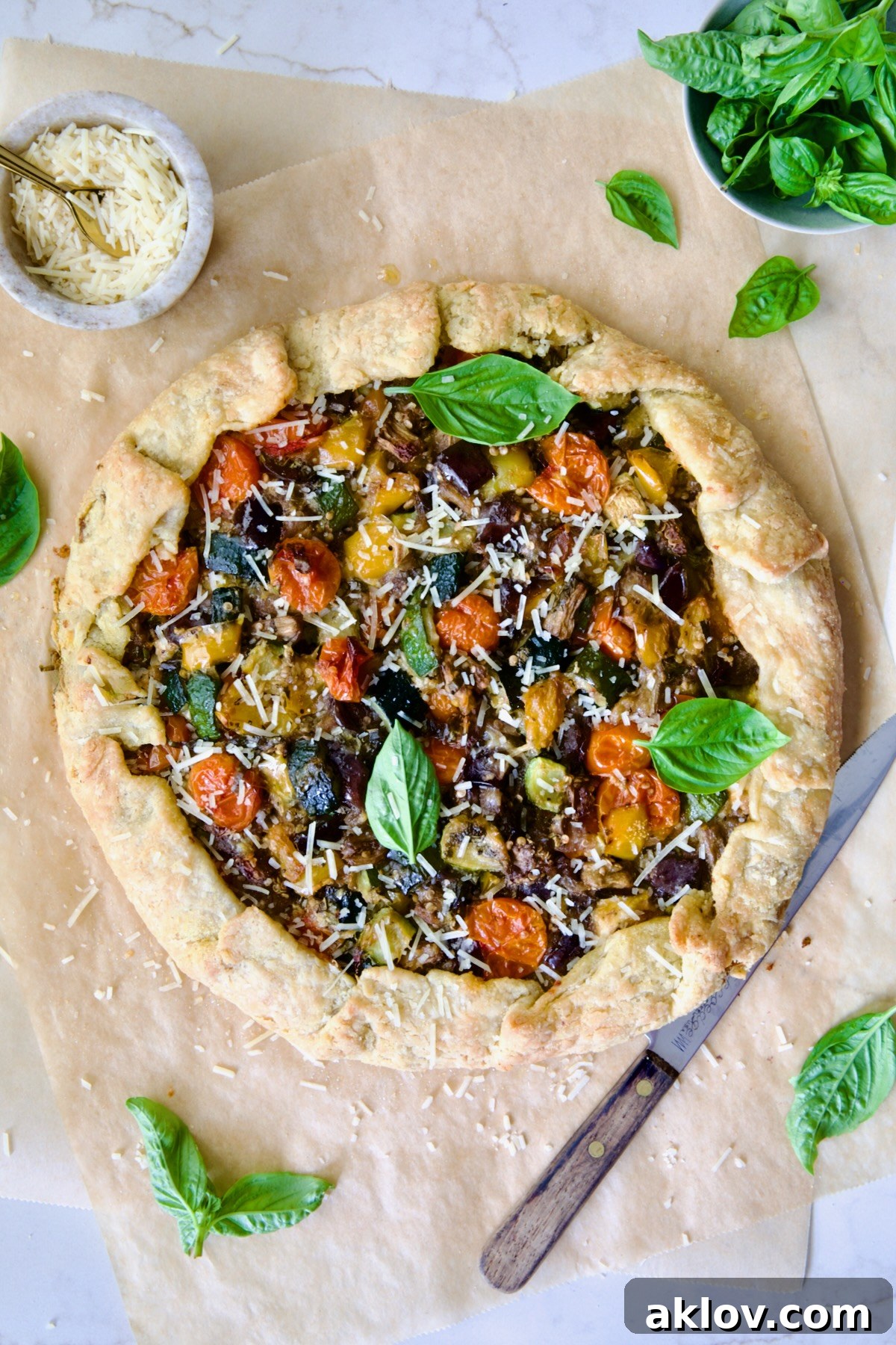 Baked Mediterranean Vegetable Galette on parchment paper garnished with fresh basil and sprinkled with Parmesan cheese.