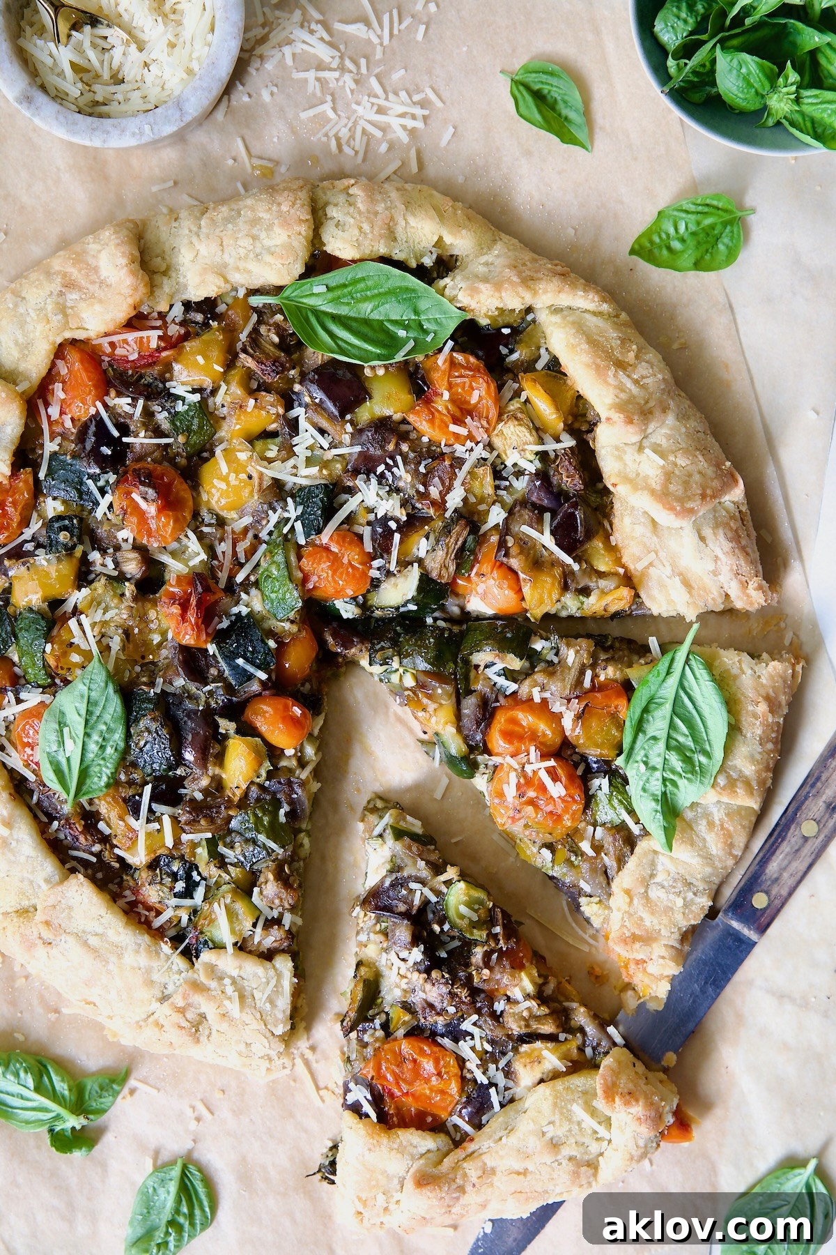 A freshly baked Mediterranean Vegetable Galette on parchment paper, elegantly garnished with fresh basil, with two slices already removed, revealing its vibrant interior.