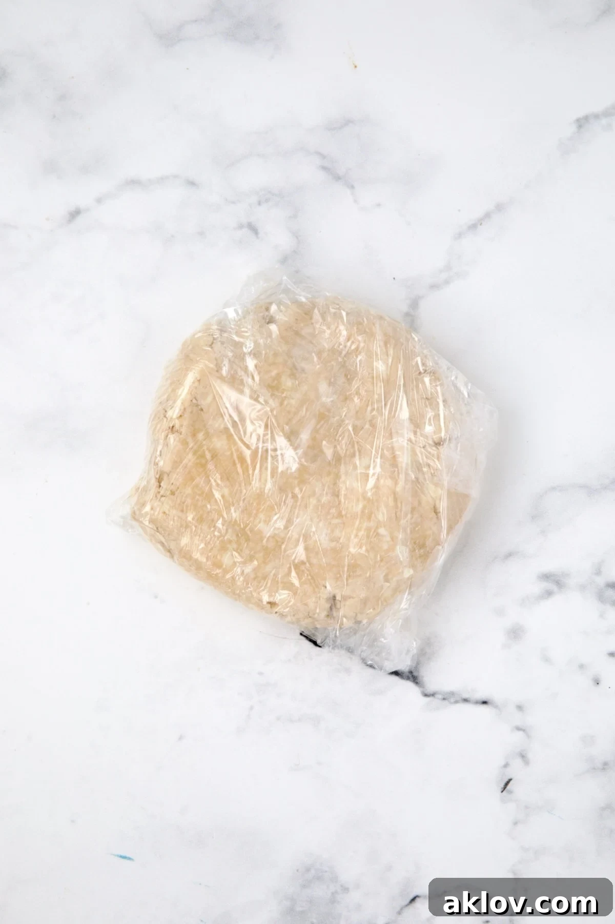 Galette dough shaped into a disk and tightly wrapped in plastic wrap, ready for chilling in the refrigerator.