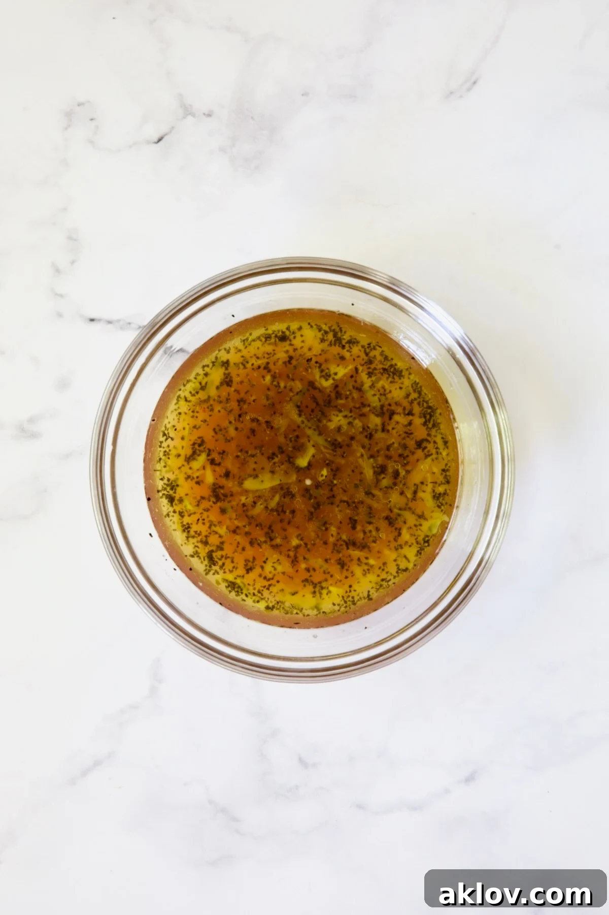 Vinaigrette in glass bowl on white marble background.