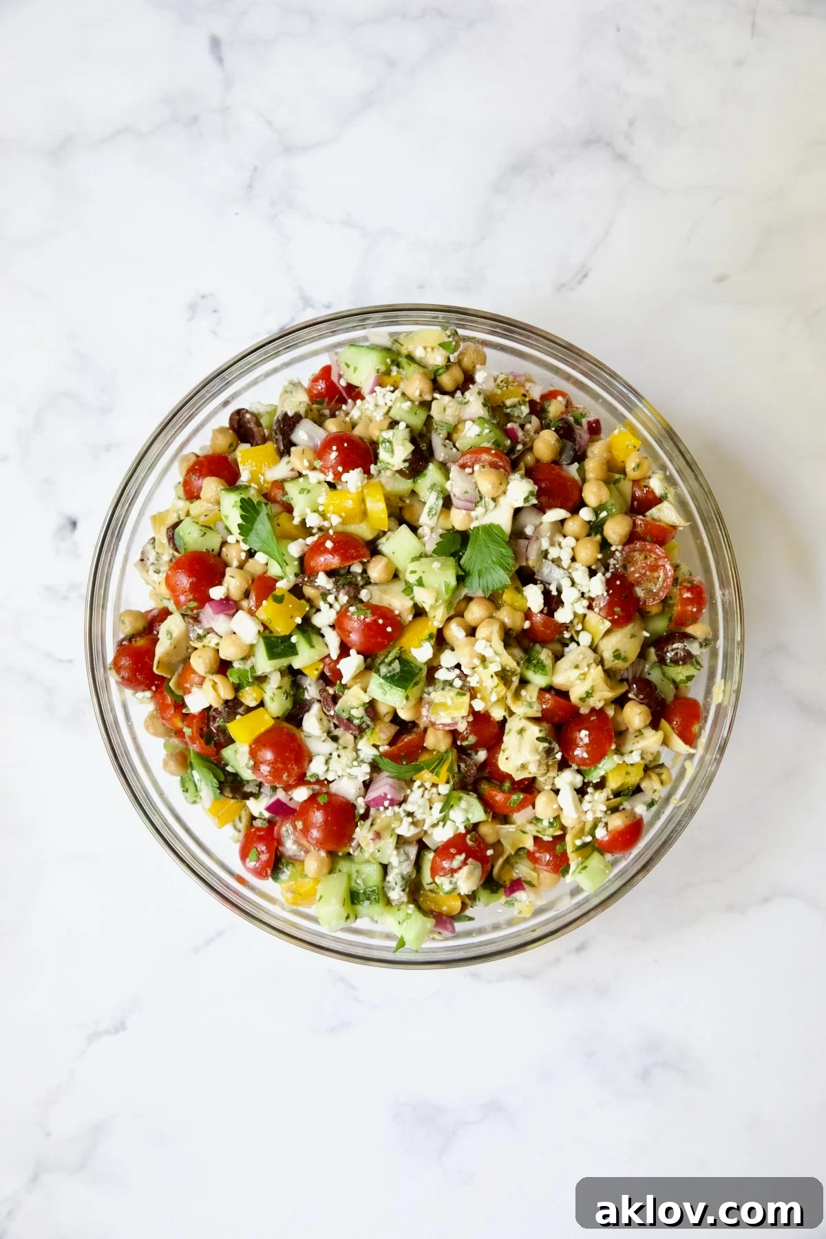Chopped salad in glass bowl on white marble background.