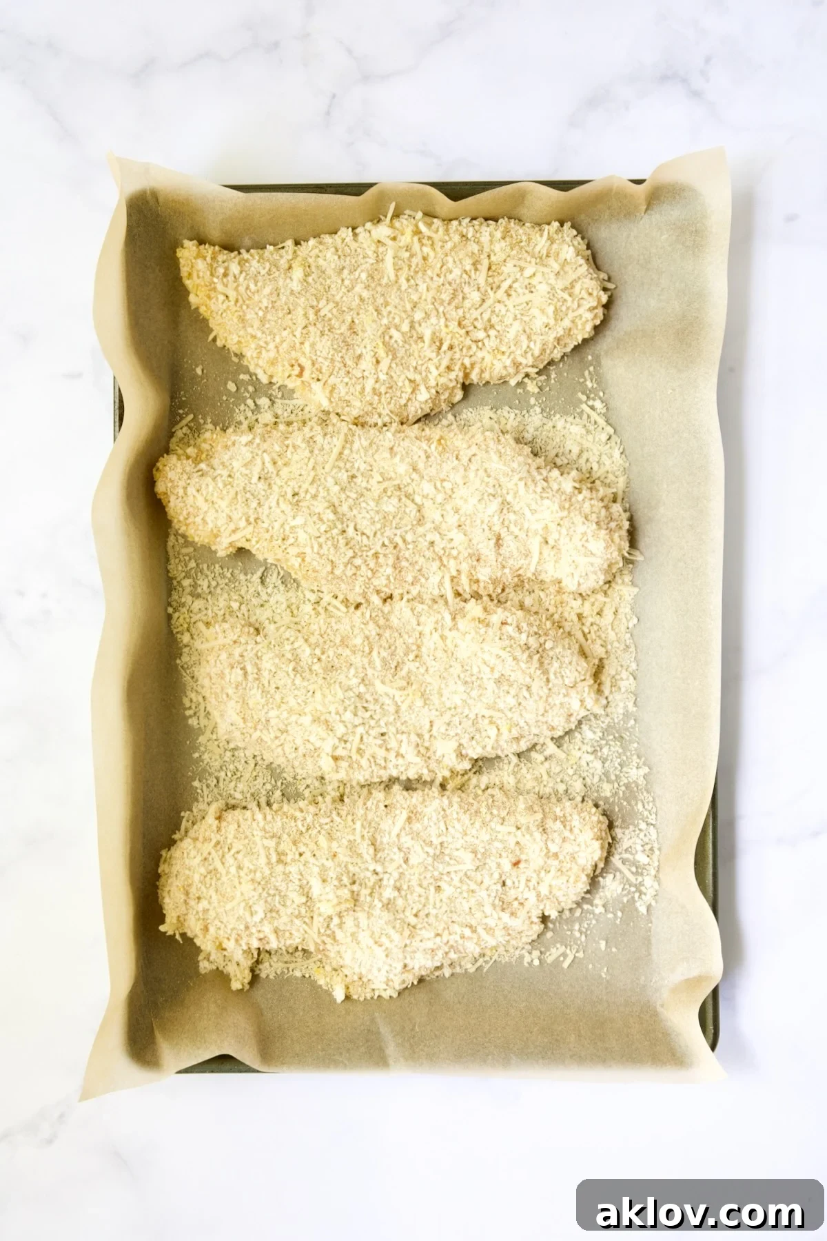Golden Crispy Milanese 14 Four prepped pieces of breaded chicken cutlets laid out on a parchment paper-lined baking sheet, ready for frying.