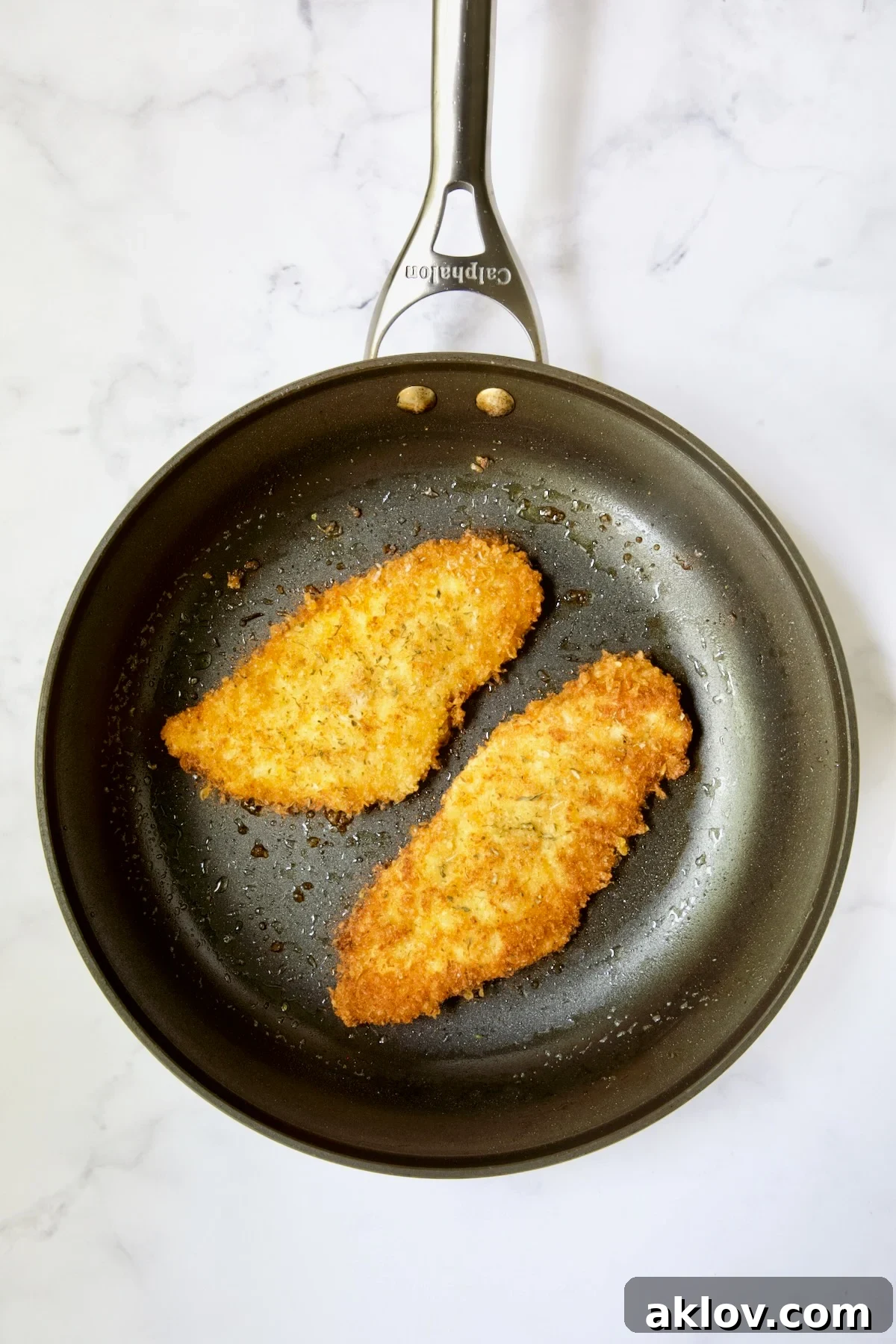 Golden Crispy Milanese 15 Two golden-brown fried chicken cutlets sizzling in a nonstick skillet with hot olive oil.