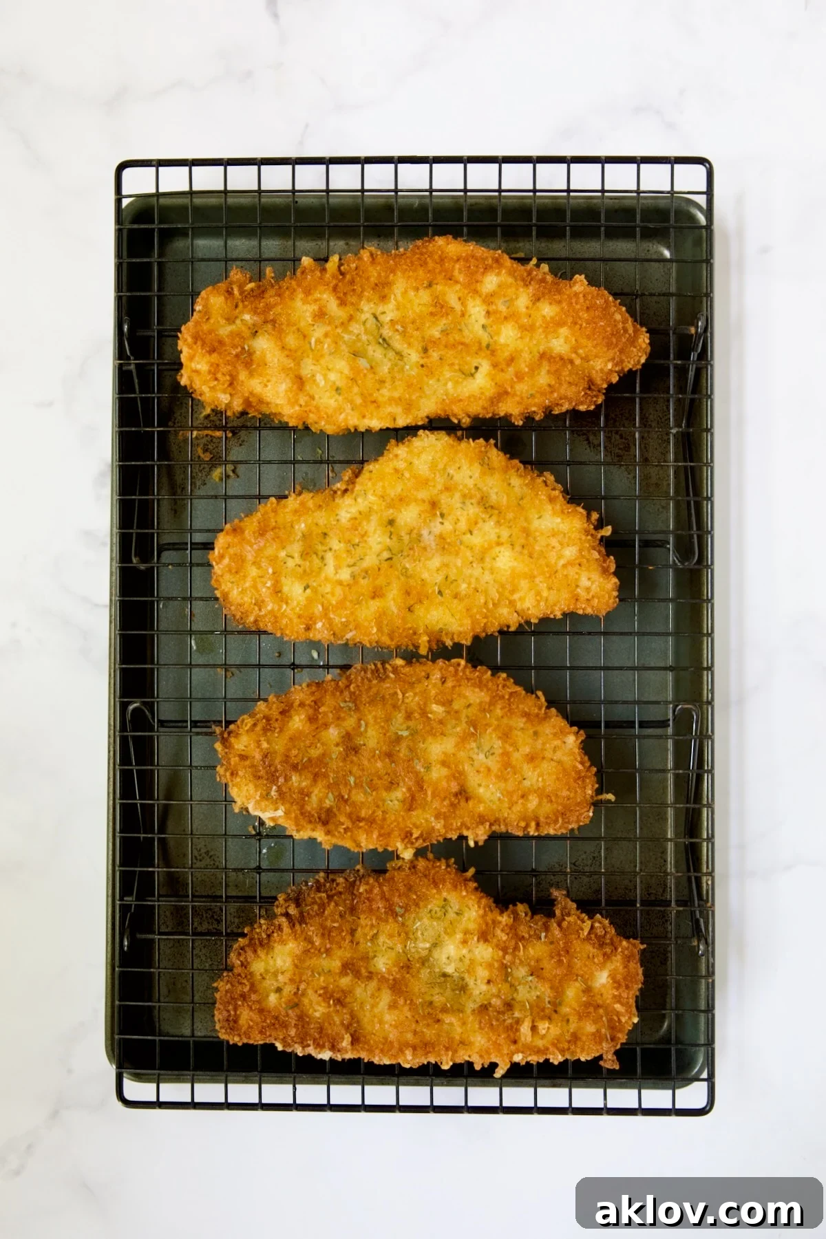Golden Crispy Milanese 16 Four pieces of perfectly fried chicken cutlets resting on a cooling rack, elevated over a baking sheet, to maintain crispiness.