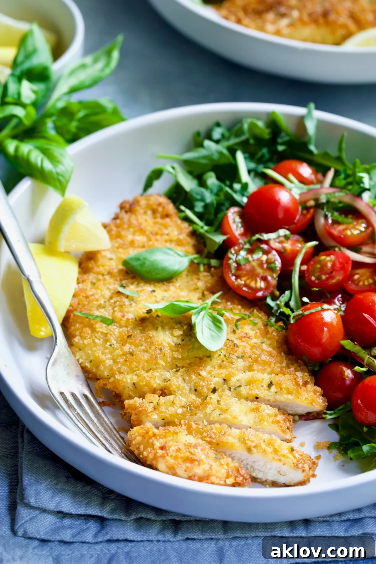 Golden Crispy Milanese 18 A close-up of a single serving of crispy Chicken Milanese with a refreshing Arugula and Cherry Tomato Salad in a white dish, ready to be enjoyed.
