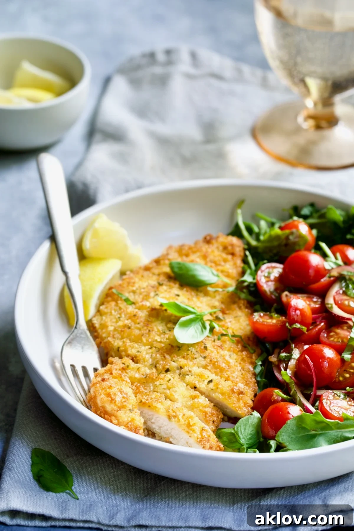 Golden Crispy Milanese 3 A single serving of golden-brown Chicken Milanese nestled beside a colorful Arugula and Cherry Tomato Salad in a white bowl.
