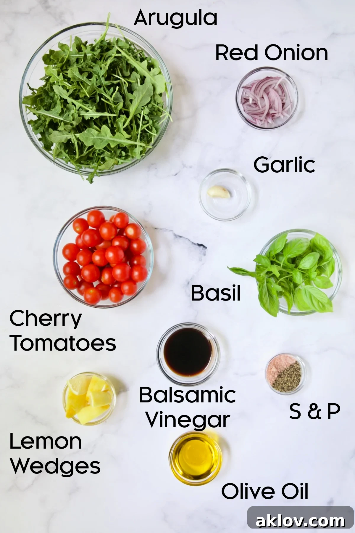 Golden Crispy Milanese 5 Glass bowls filled with fresh ingredients for Arugula and Cherry Tomato Salad: halved tomatoes, red onion, garlic, basil, and bottles of olive oil and balsamic vinegar.